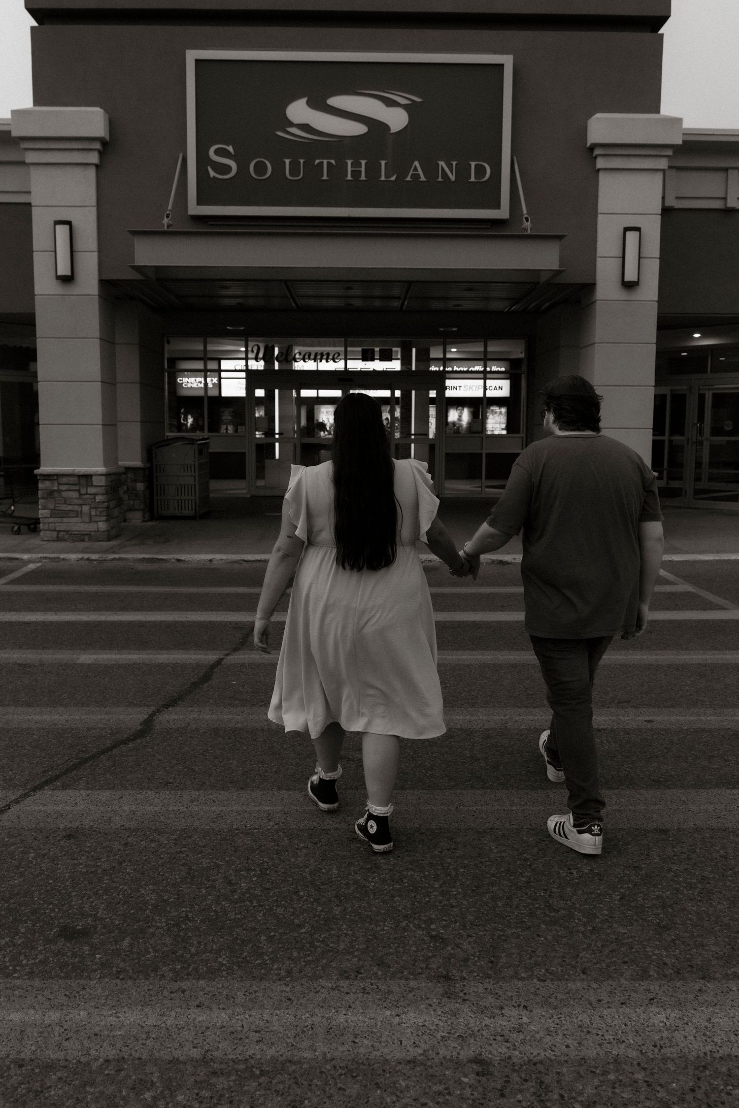 Black and white photo of a couple holding hands walking toward Southland mall entrance.