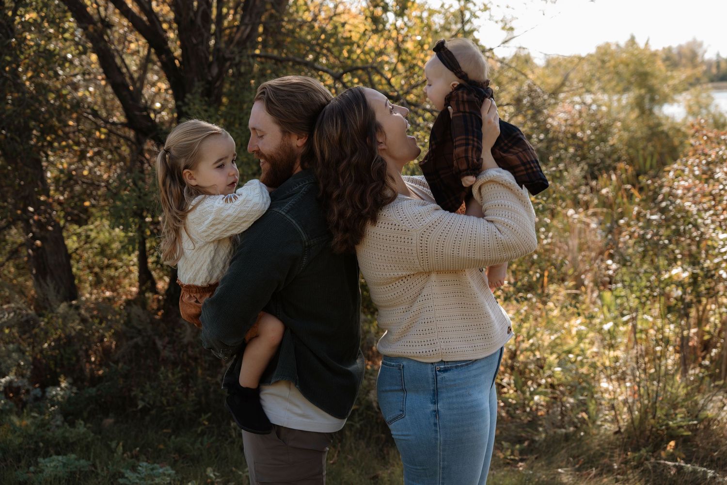A happy family of four enjoys an outdoor autumn photo session among colorful fall foliage.