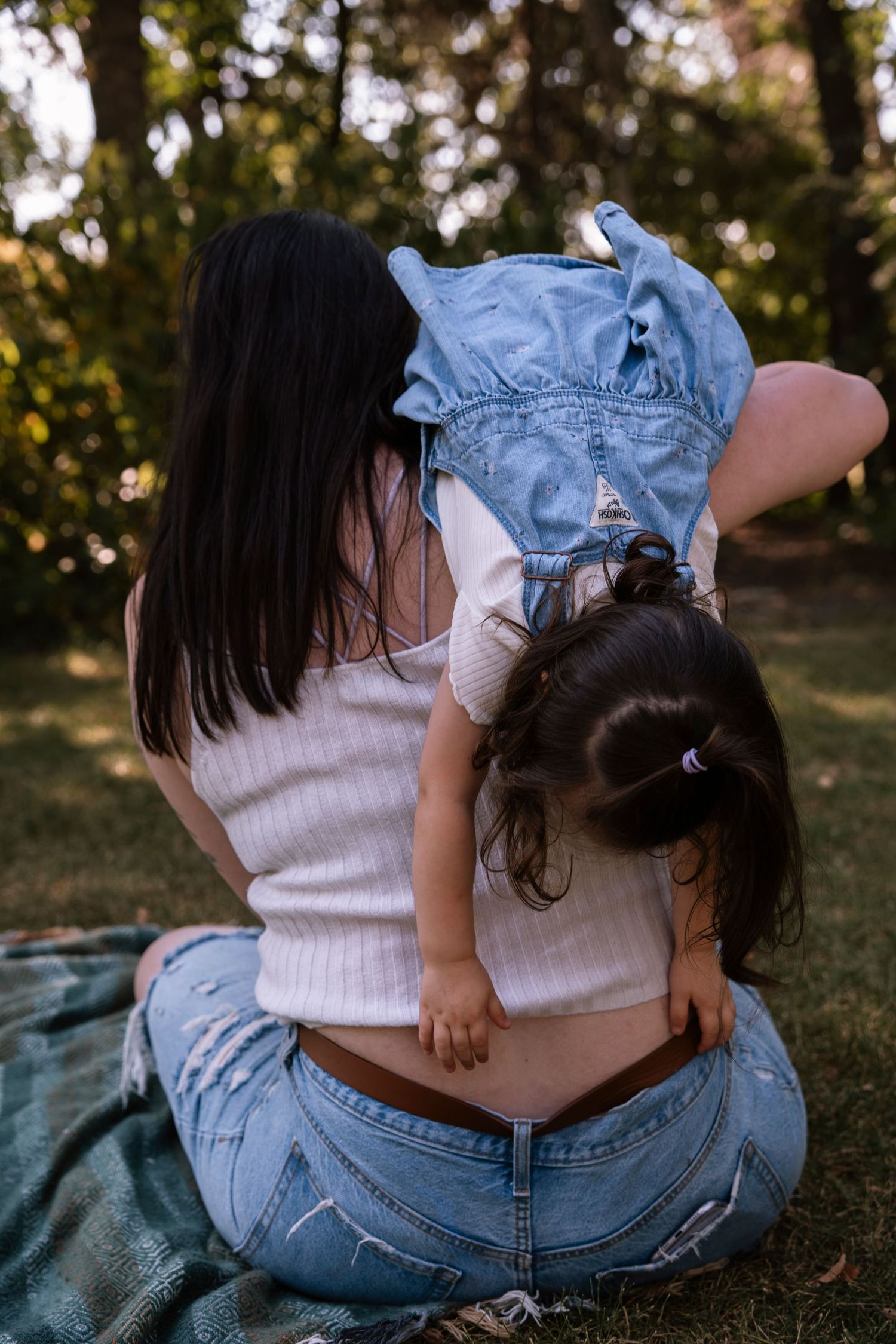 A parent and child wearing matching white tops and denim sit together on a blanket outdoors during a sunny day.Regina Saskatchewan Family