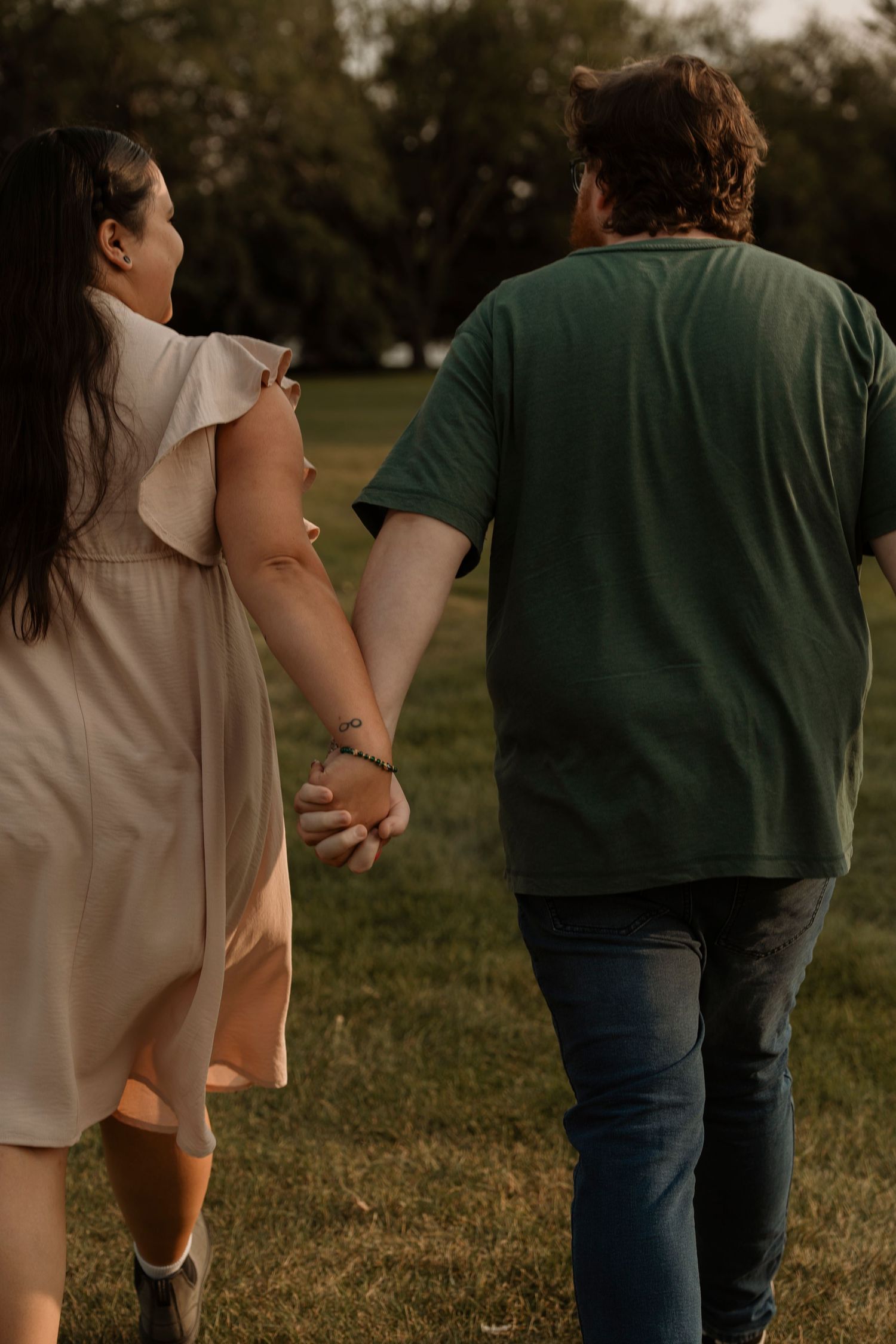 Couple holding hands walking through a green park, woman in white dress and man in green shirt.