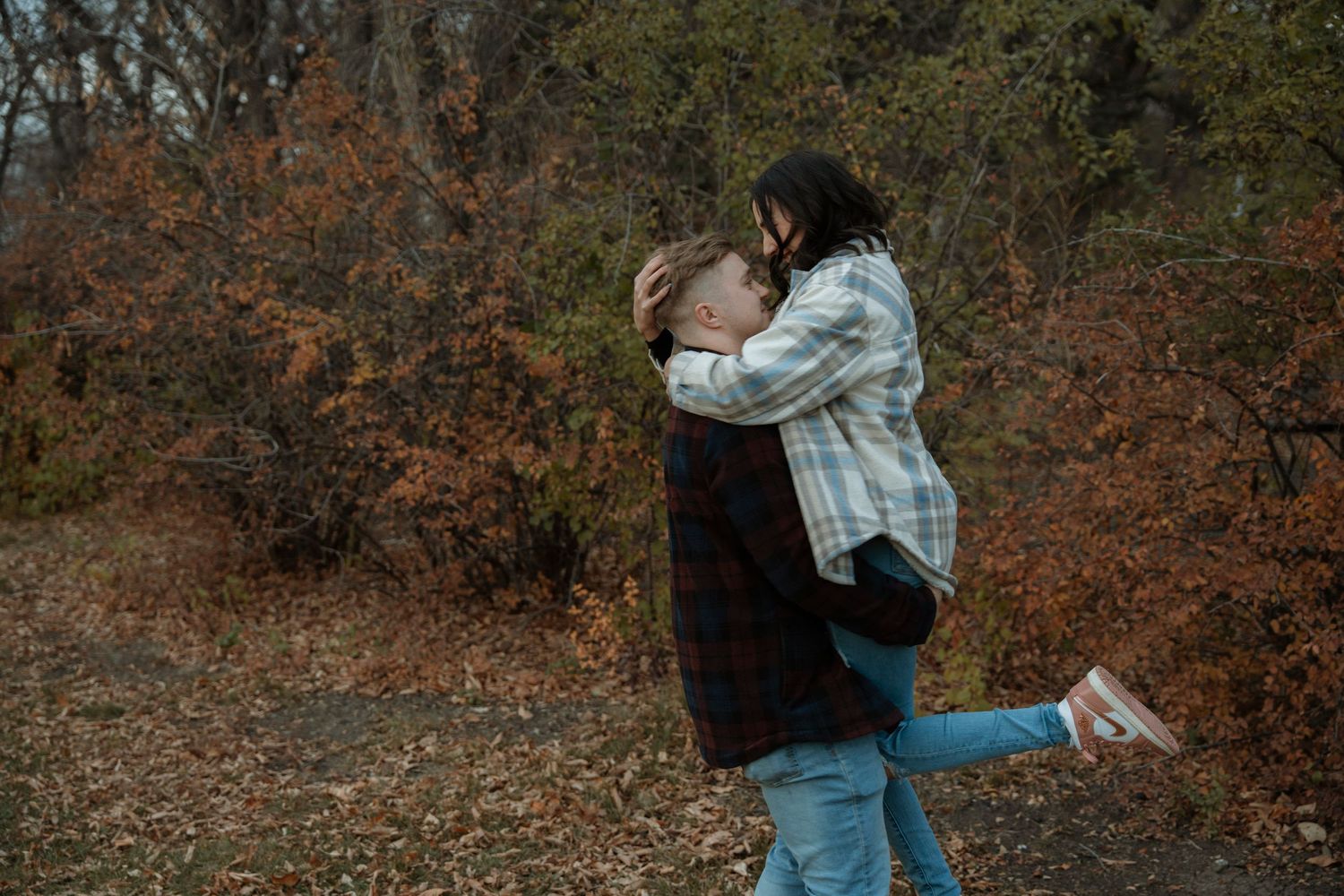 Couple embracing in autumn forest, man lifting woman among colorful fall foliage outdoors.