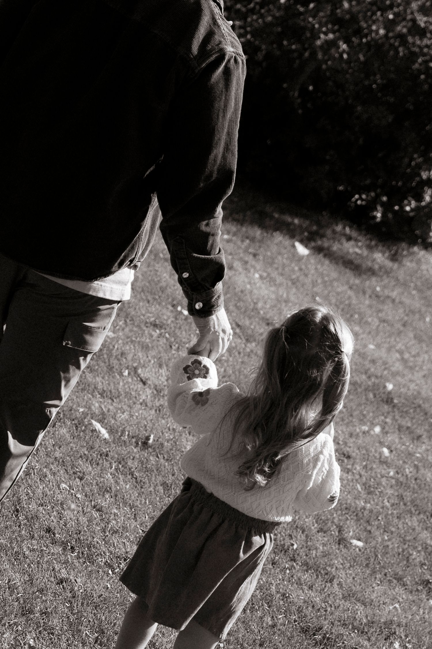 Black and white photo of adult holding child's hand outdoors, viewed from above on grass.