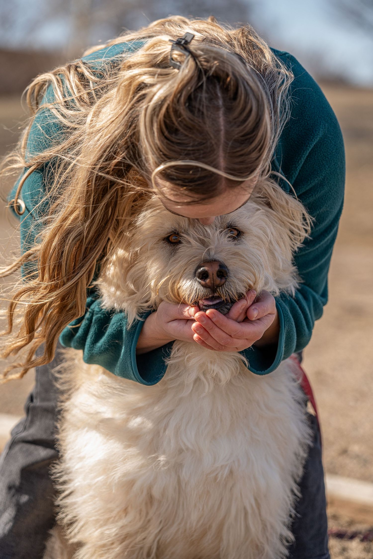 Young girl with long hair hugging a fluffy white dog outdoors on a sunny day.Saskatchewan Photographer.