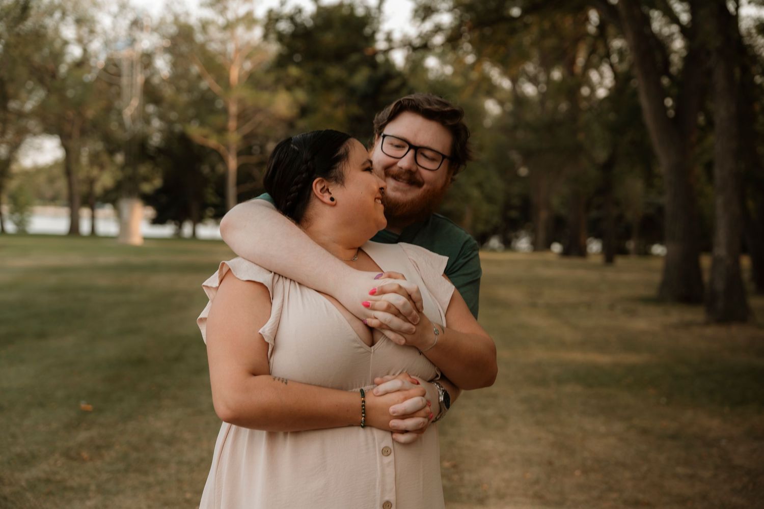 Couple embracing and laughing together in a lush green park during golden hour engagement photo session.
