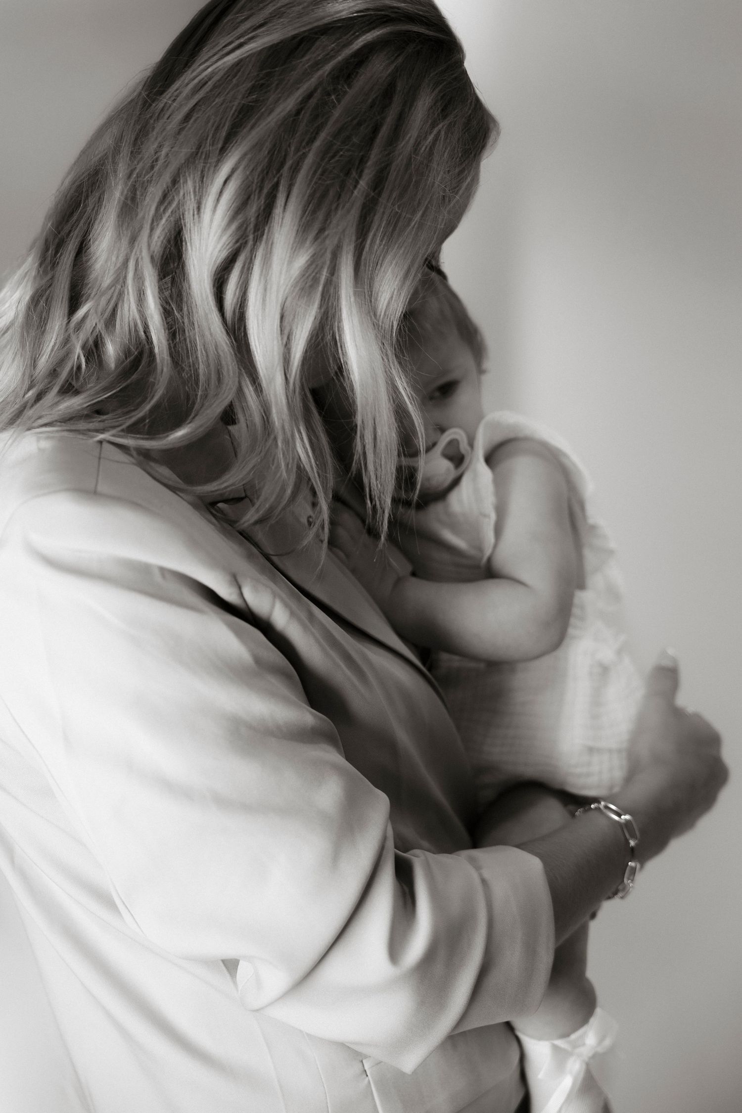 Black and white photo of a blonde woman tenderly cradling a newborn baby against her chest.