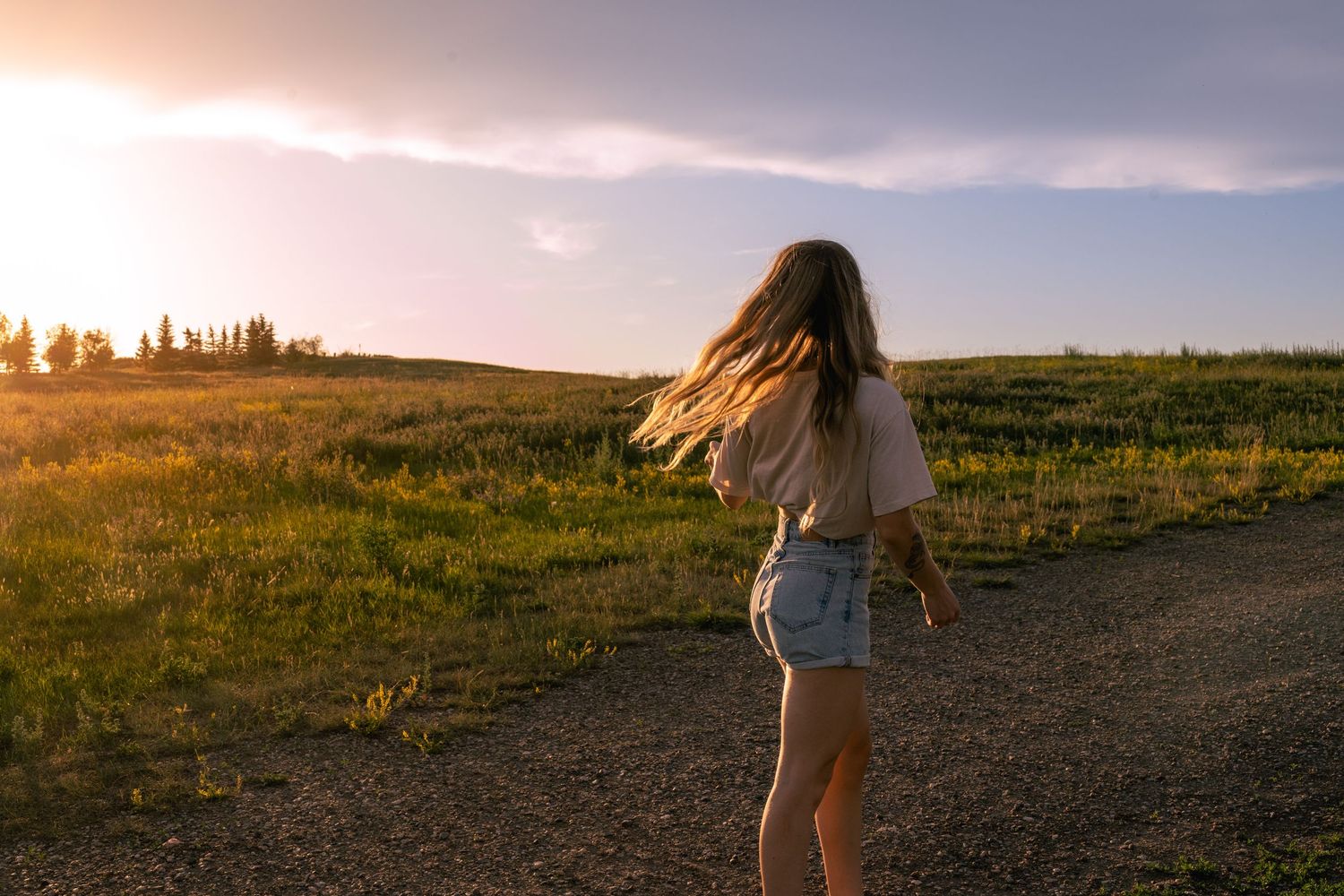 Person walking along a grassy hilltop path at sunset with golden light illuminating the landscape.