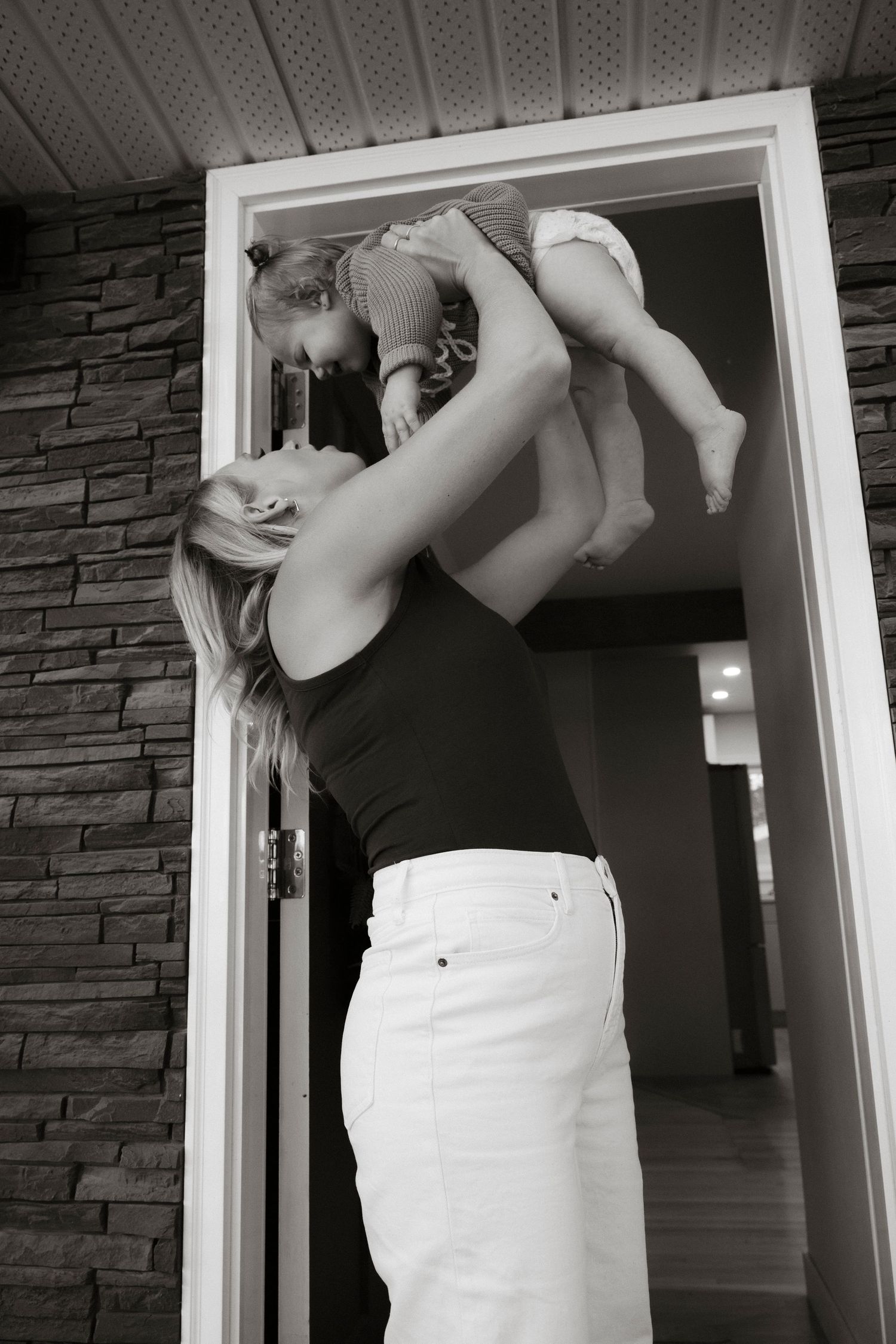 Black and white photo of a mother lifting her baby in a doorway, sharing a joyful moment together.