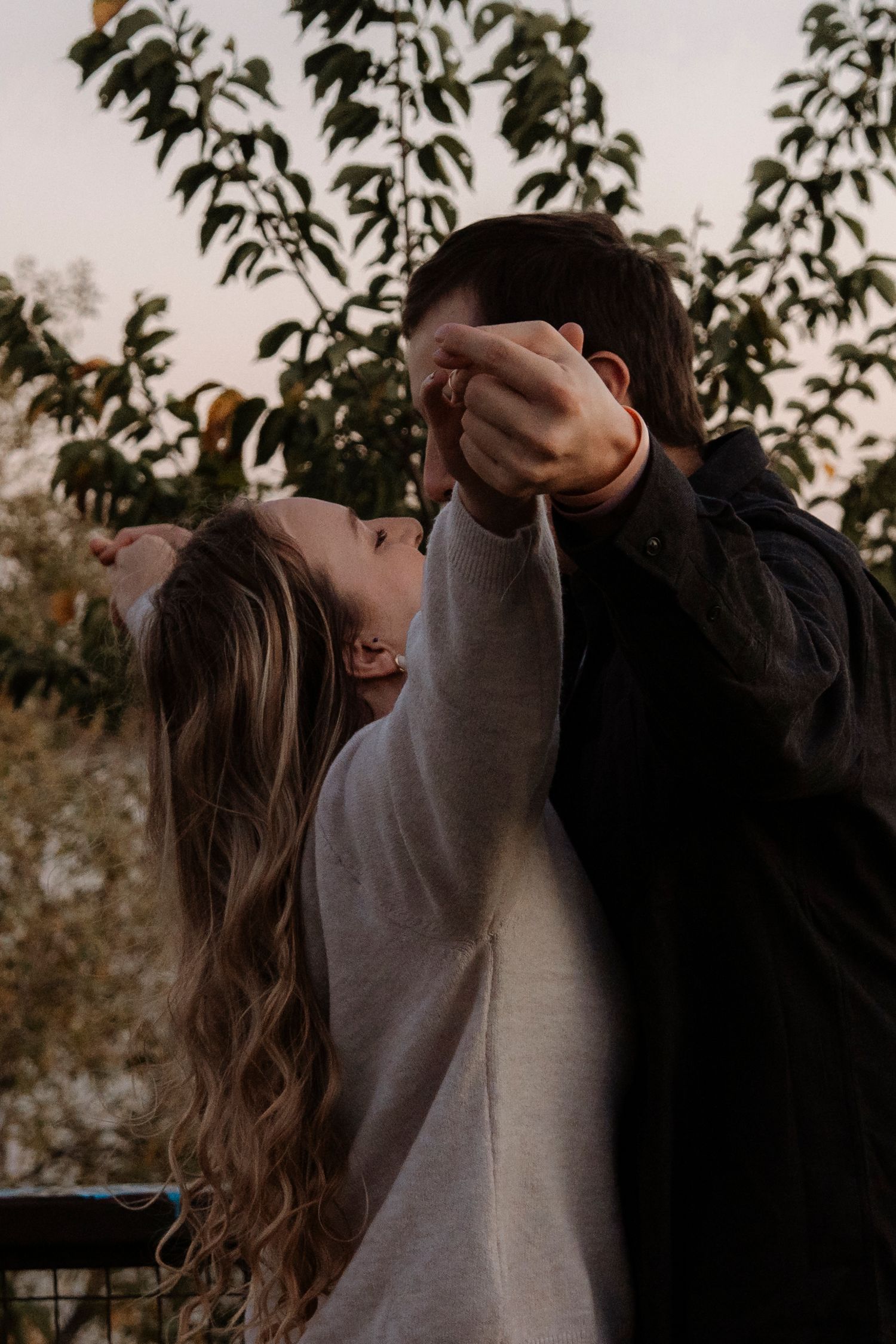 A couple sharing a romantic dance outdoors beneath a fruit tree at dusk, the woman leaning back joyfully.