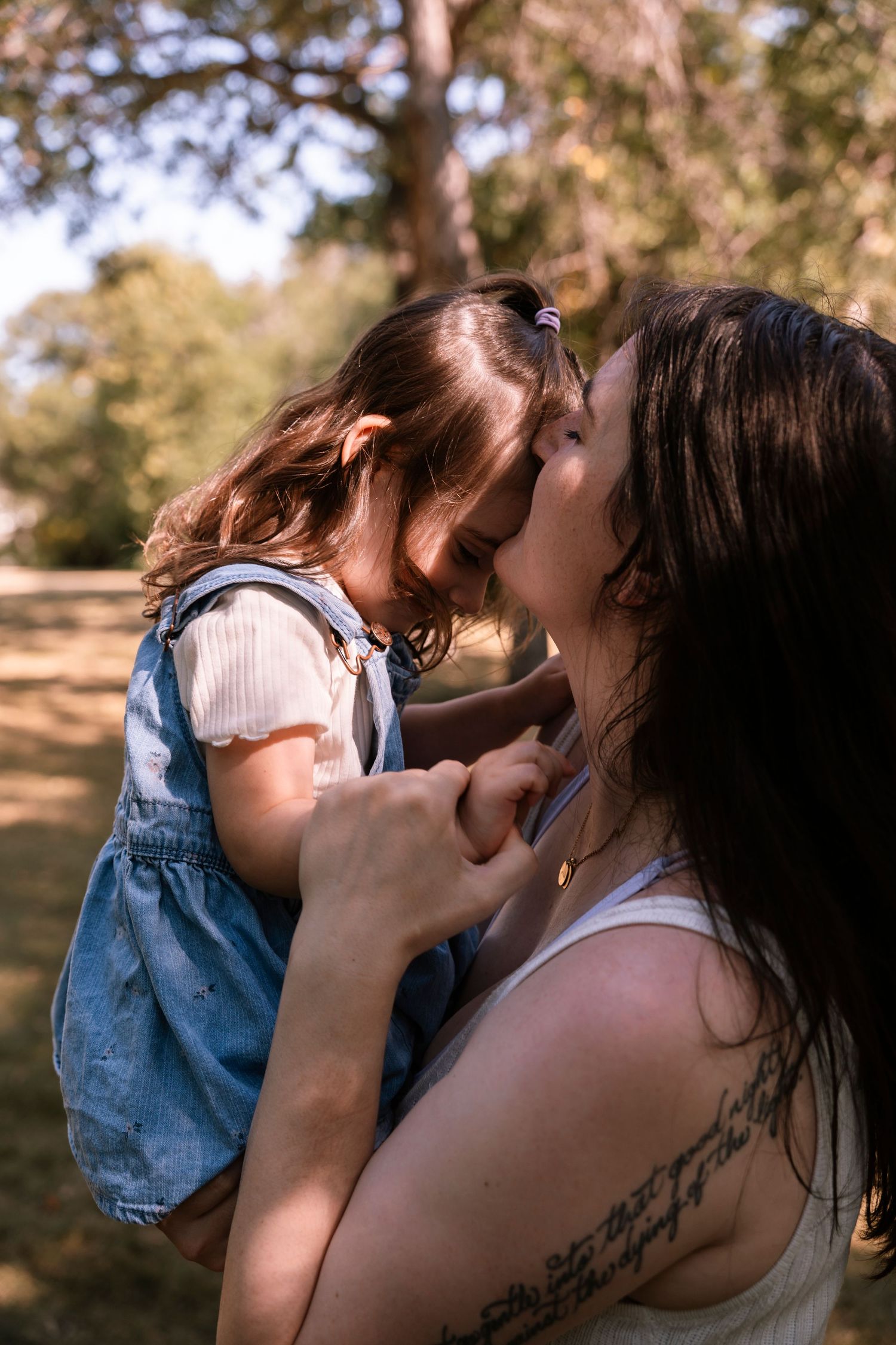 Two people share an intimate moment outdoors in golden sunlight among trees. Regina Saskatchewan candid portrait photographer.