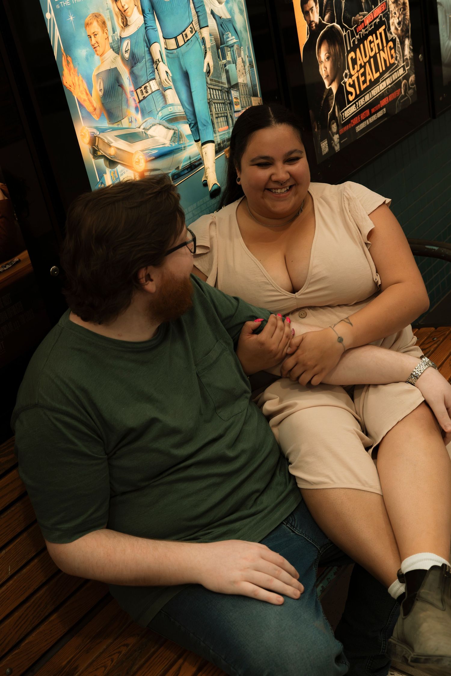 A couple smiling and holding hands while seated together in front of movie posters in a cozy venue.