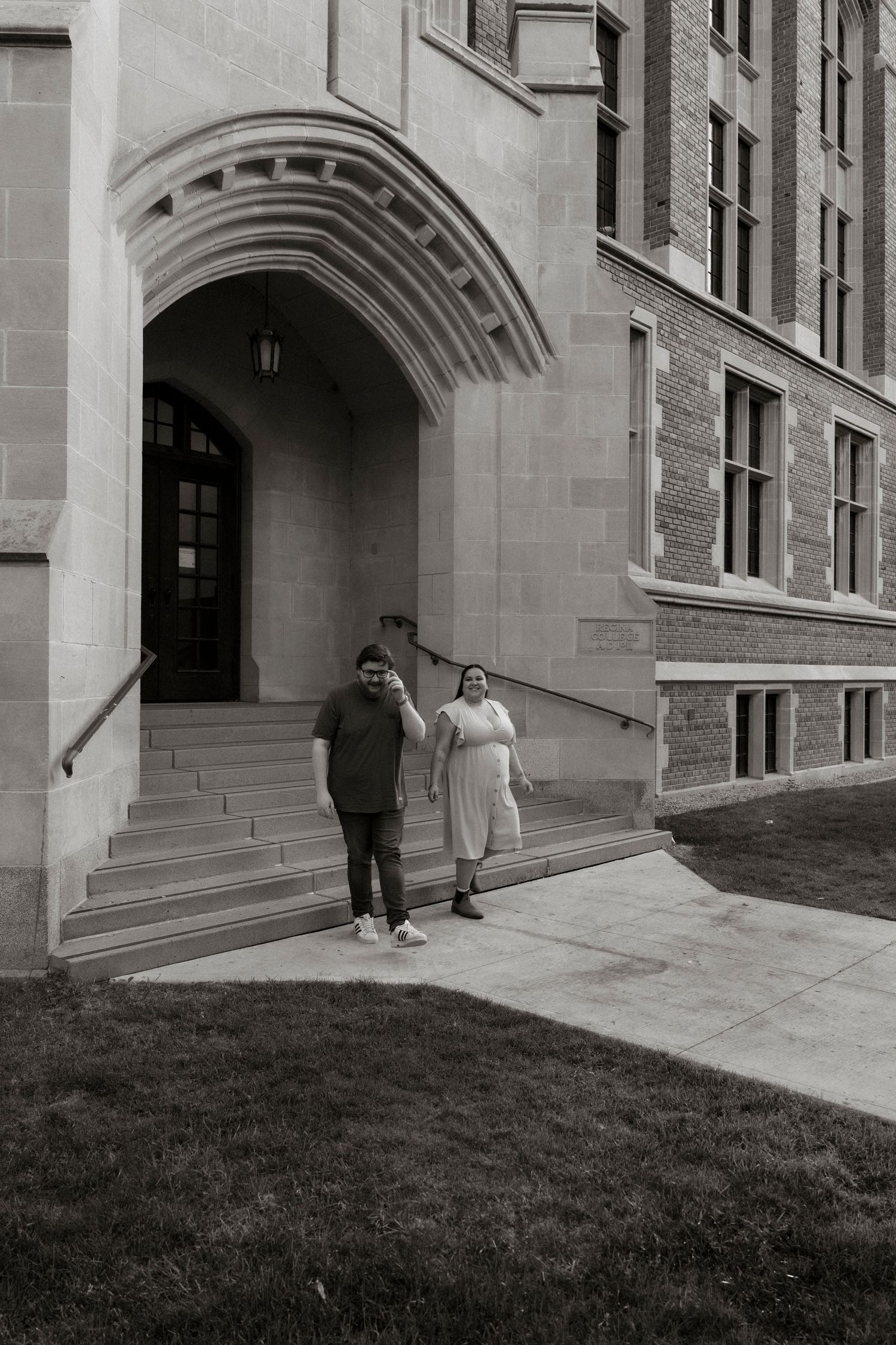 Black and white photo of two people standing at the entrance of a historic stone building with an arched doorway.