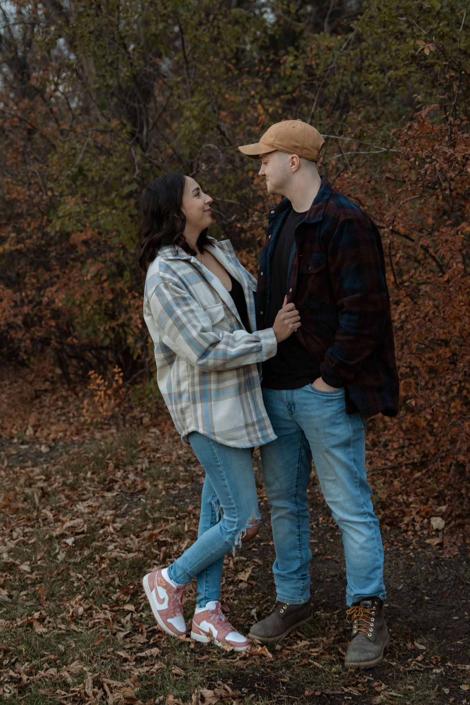 Young couple in casual fall outfits holding hands while facing each other among autumn foliage.