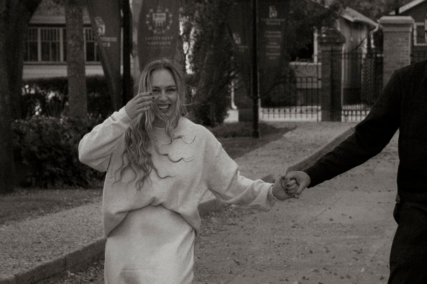 Black and white photo of a smiling woman in white outfit holding hands with a man outdoors.