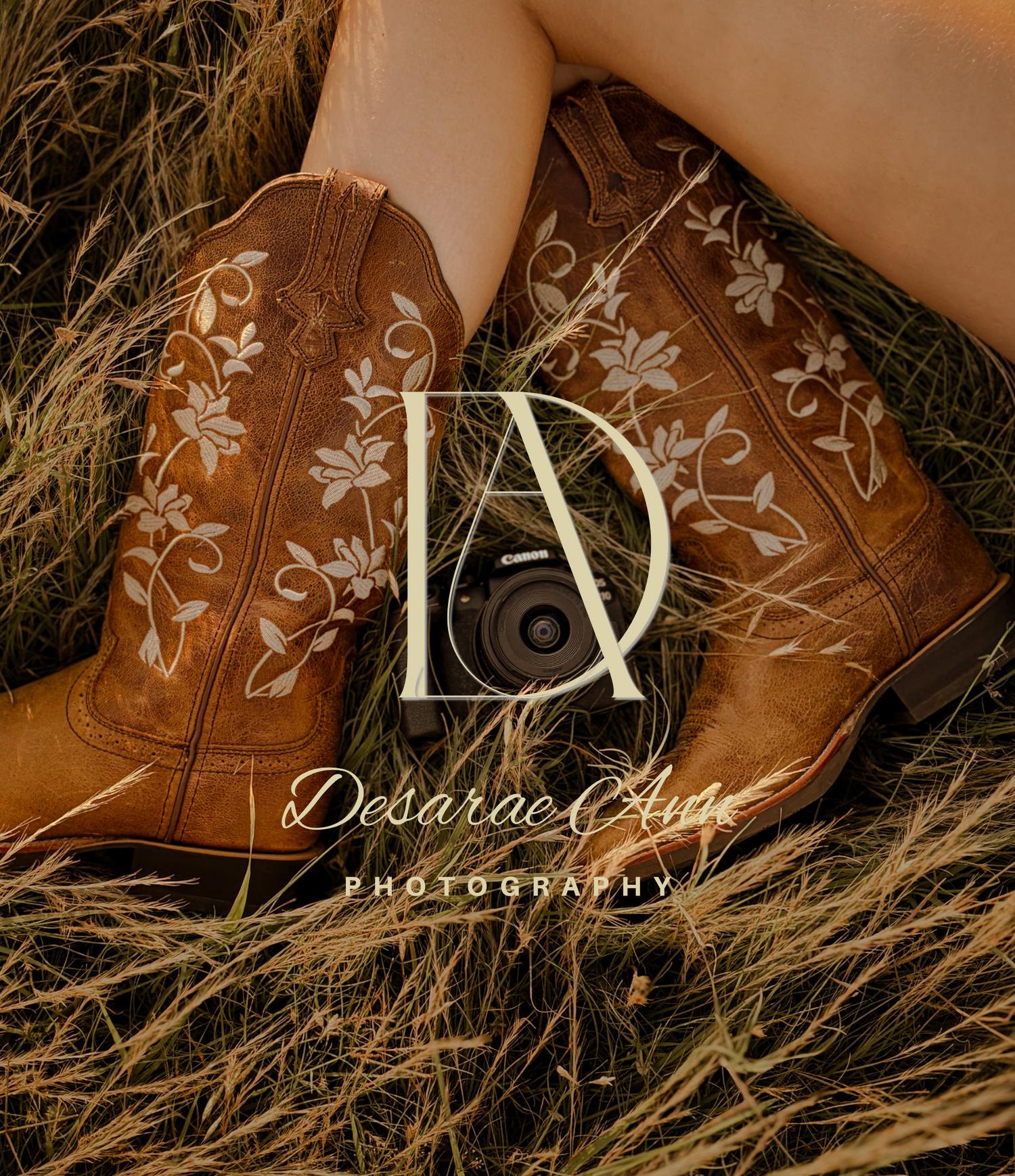 Brown cowboy boots with floral embroidery resting in dry grass, featuring Desarae Ann Photography logo overlay. Branding inspo