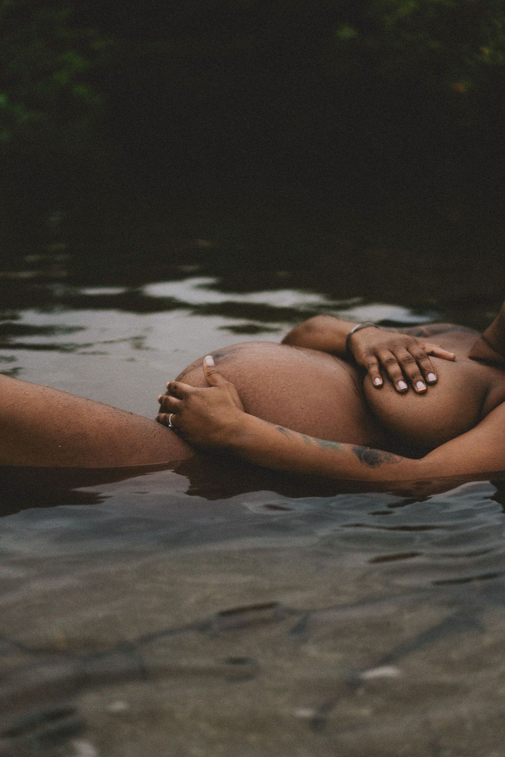 A person floats peacefully in dark water wearing body jewelry, creating a serene and artistic composition.