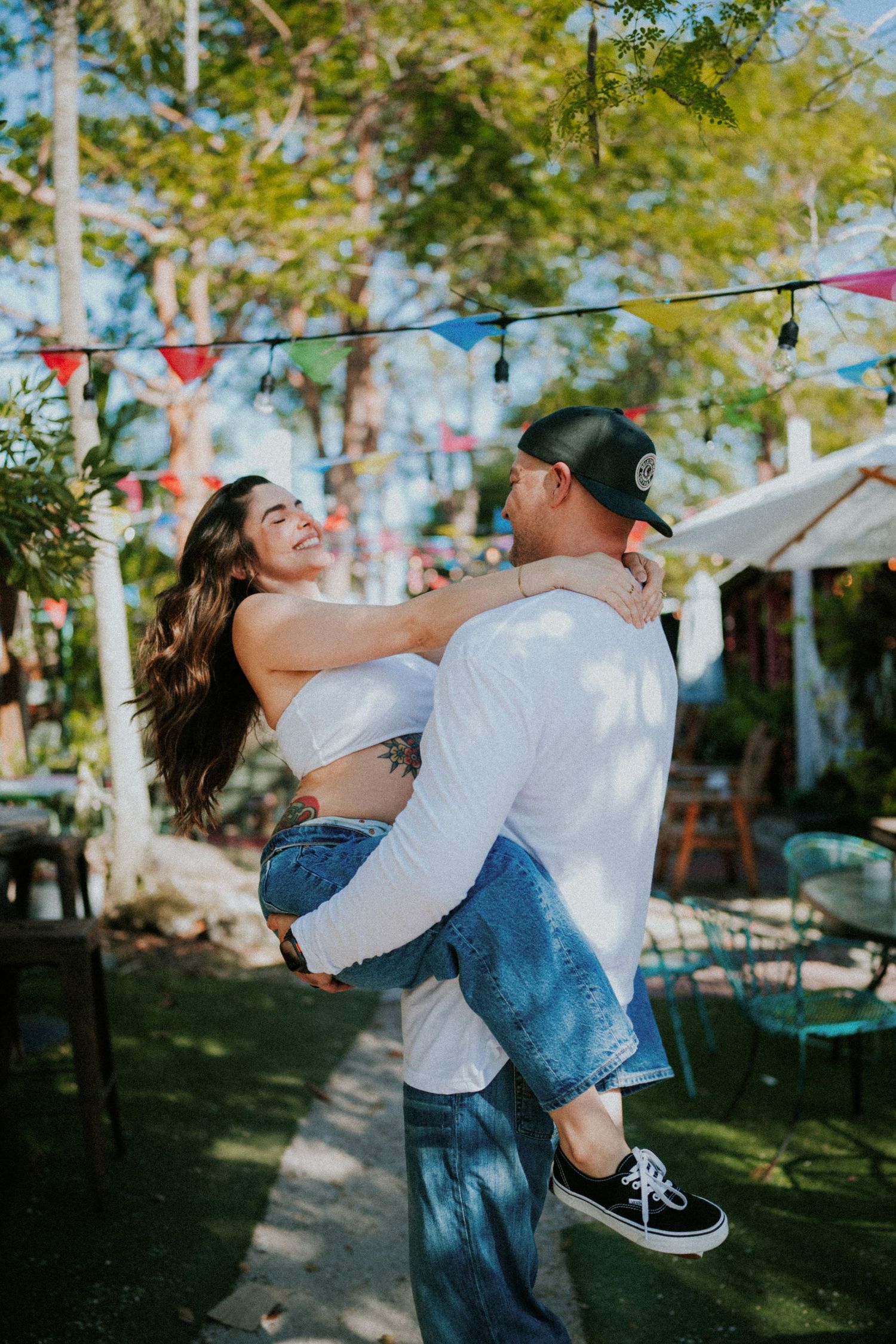 A couple spins joyfully together under colorful bunting flags at an outdoor celebration.
