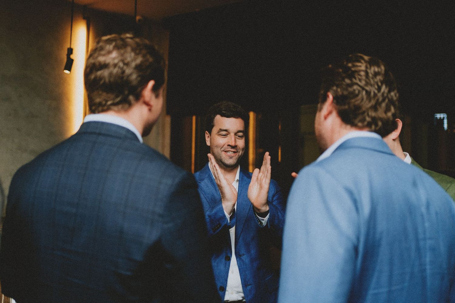 Groom clapping hands with groomsmen in blue suits before wedding ceremony indoors.