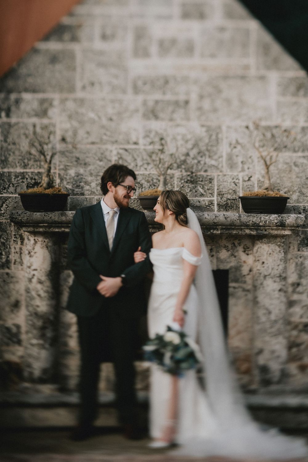Artistic black and white wedding portrait against a textured stone wall.