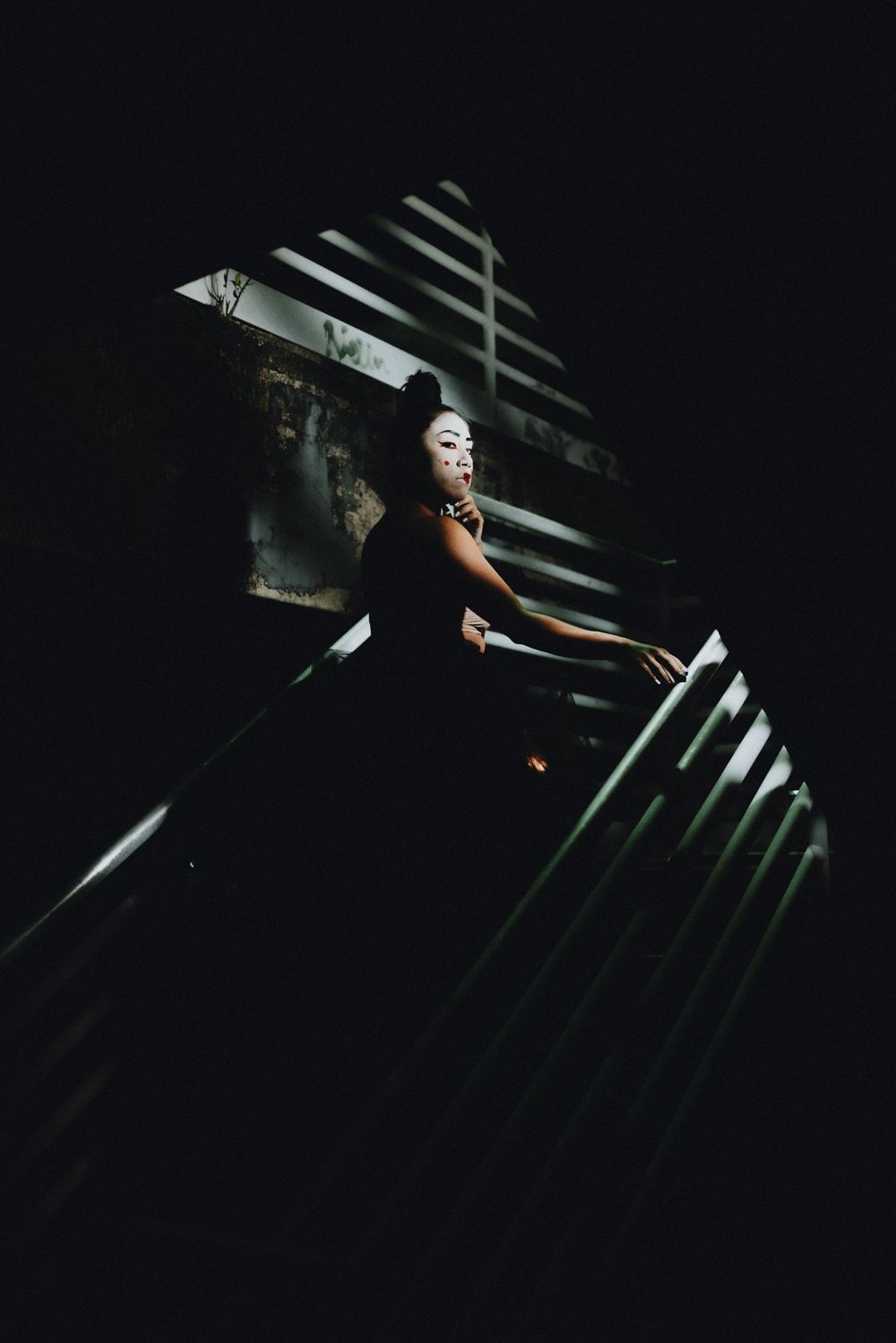 White mask visible through dramatic slats of light and shadow in dark setting.