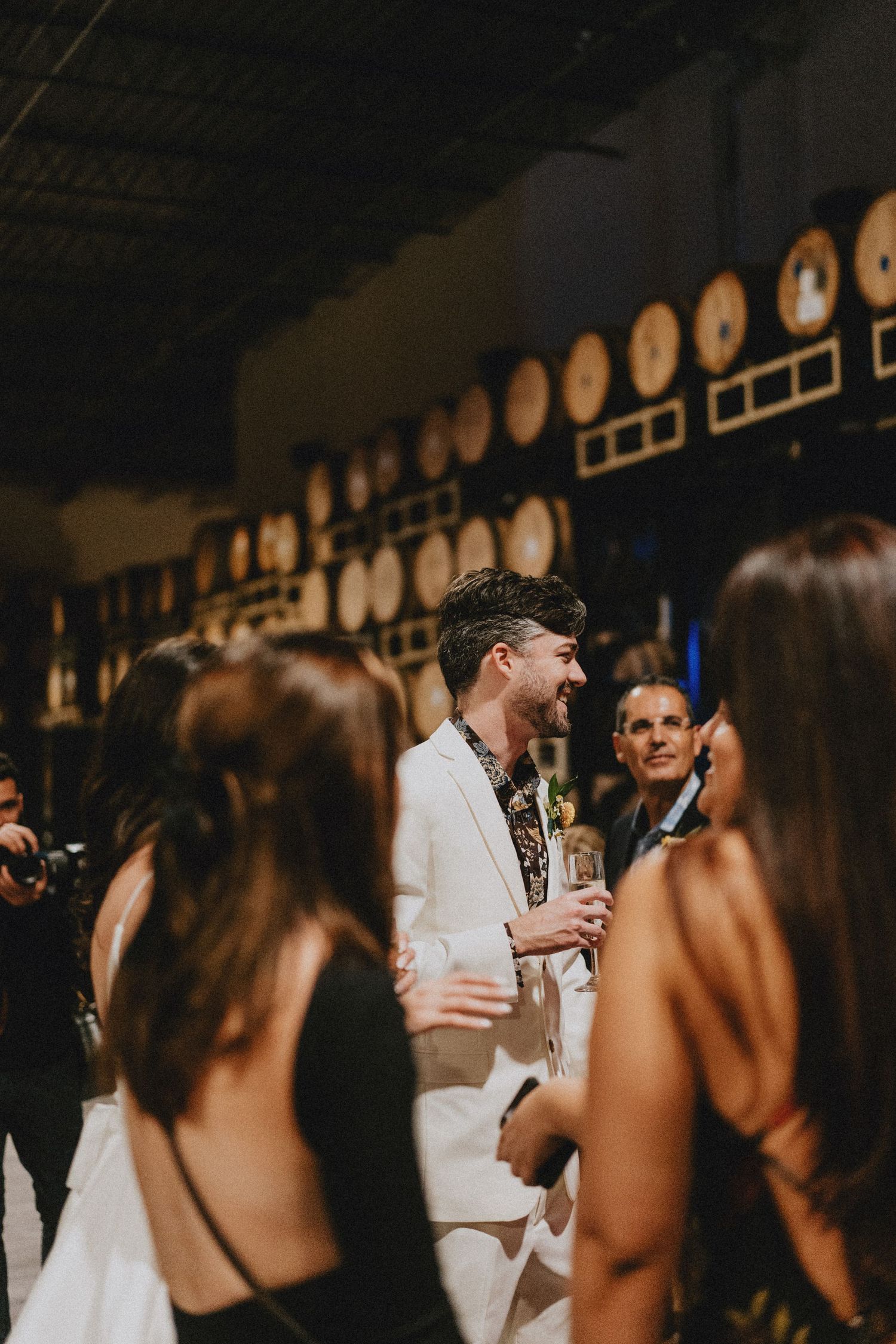 Man in white suit smiling and holding champagne at an elegant evening reception venue.