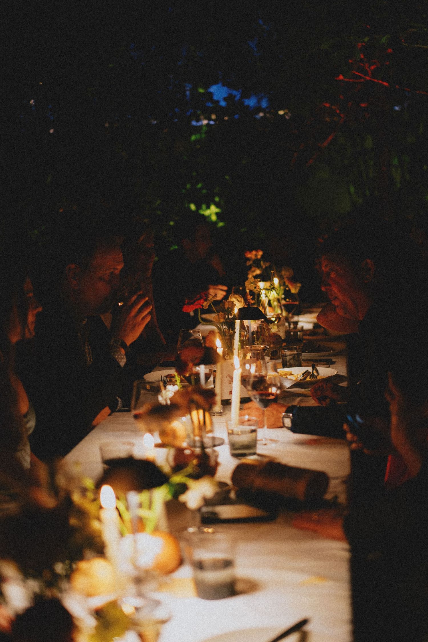 Wedding guests dining by candlelight at an elegant outdoor evening reception table.