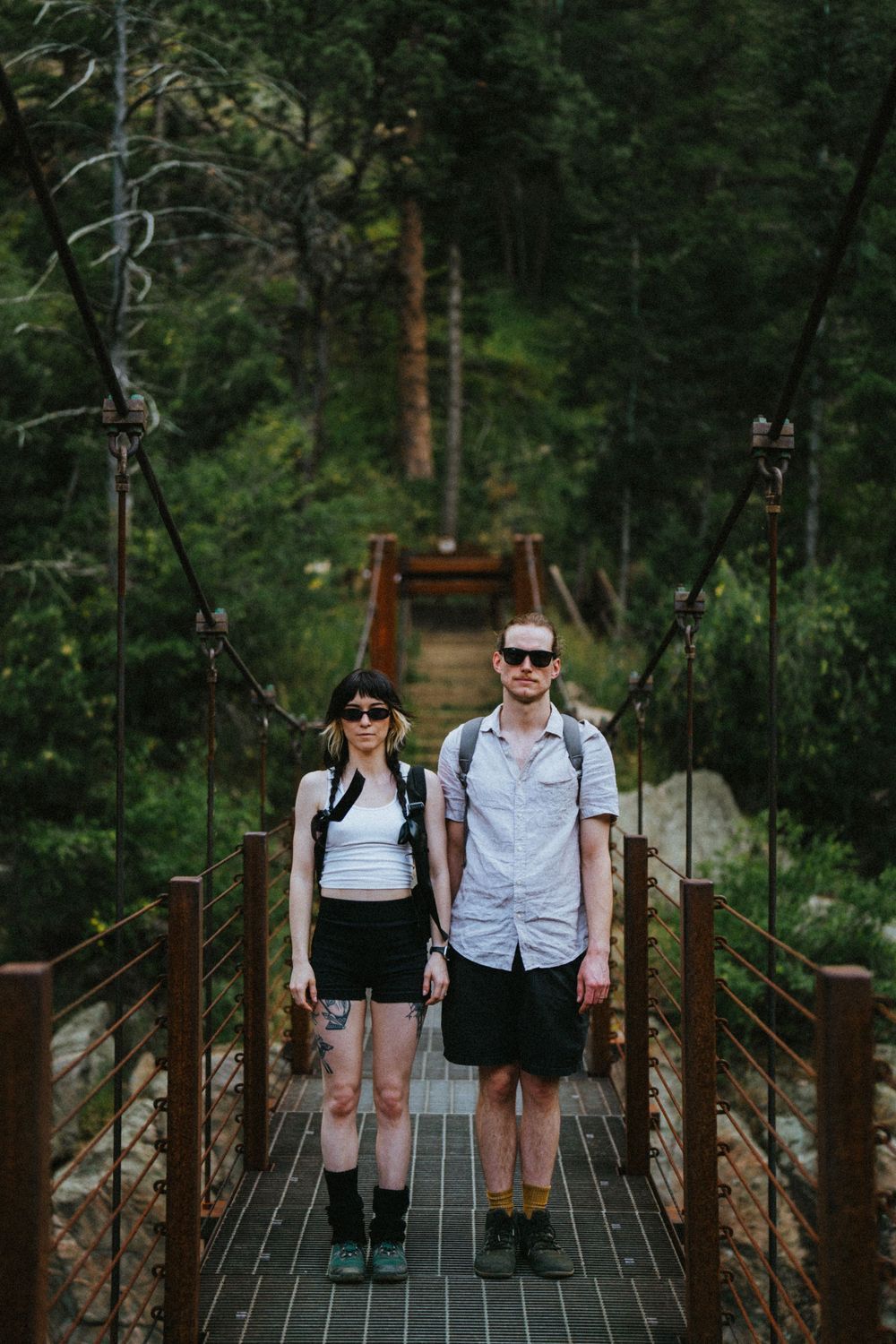 A casual couple sitting together on a wooden suspension bridge in a lush forest setting.