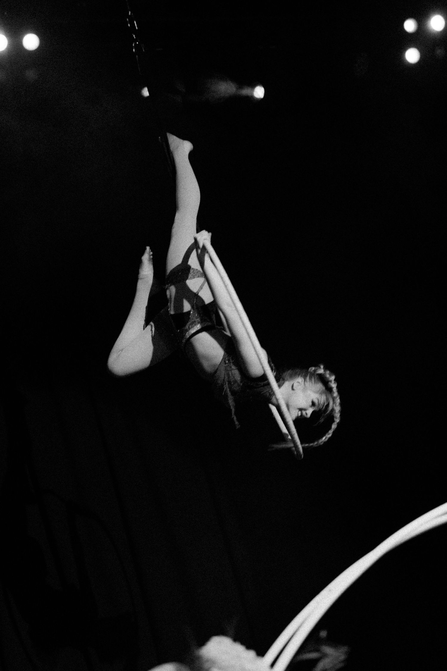 Black and white photo of an aerial silk performer gracefully suspended upside down on stage with dramatic lighting.