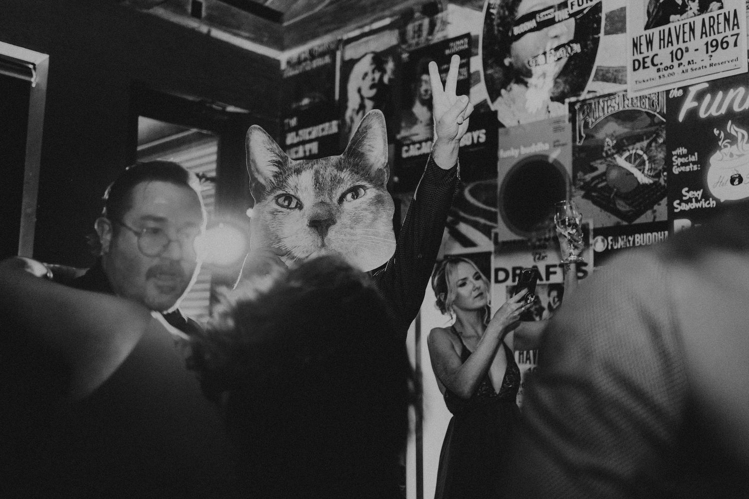 Black and white photo of wedding guests dancing near a large cat poster at a fun reception.