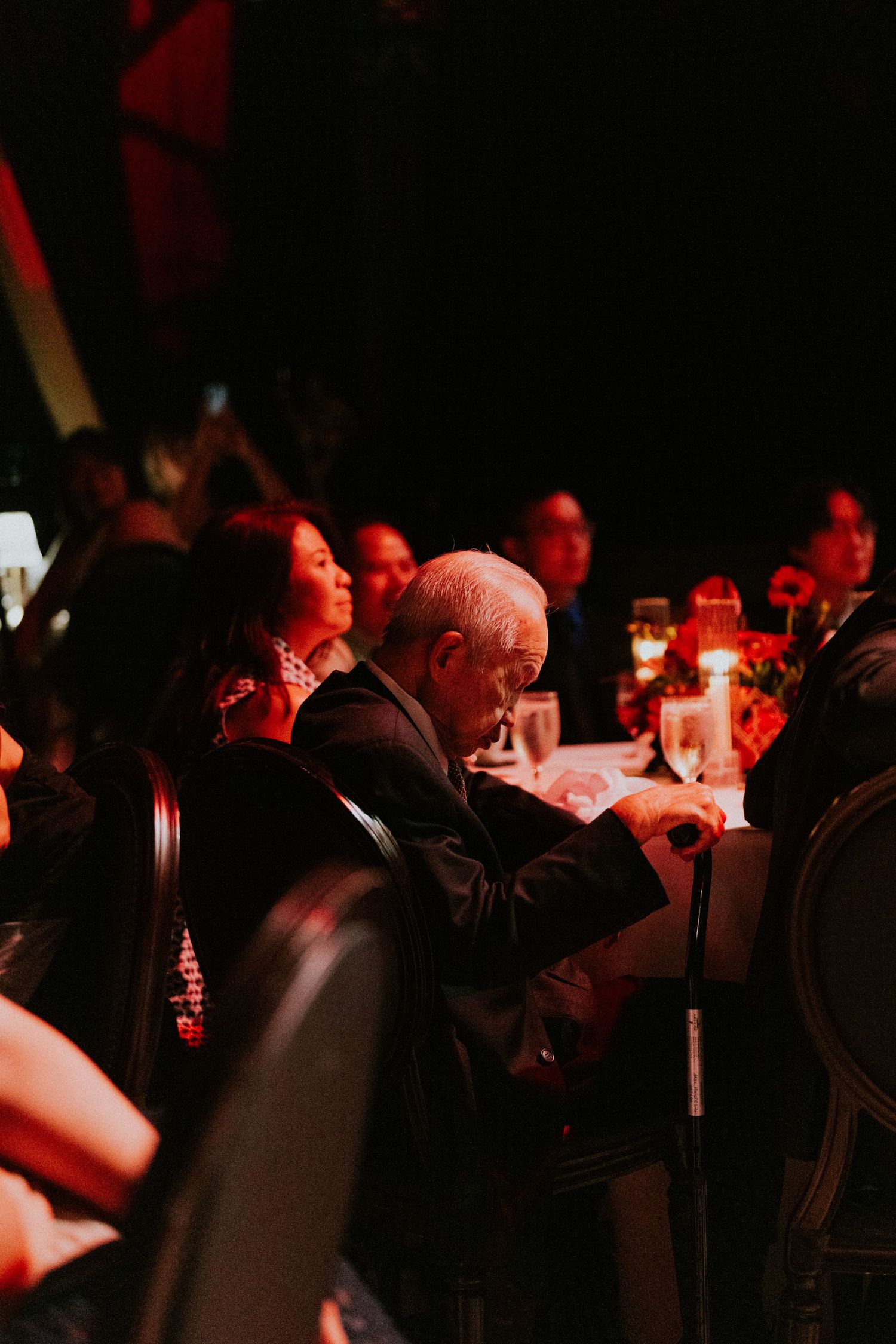 Guests seated at elegantly decorated tables with red candlelight at a formal evening gala event.