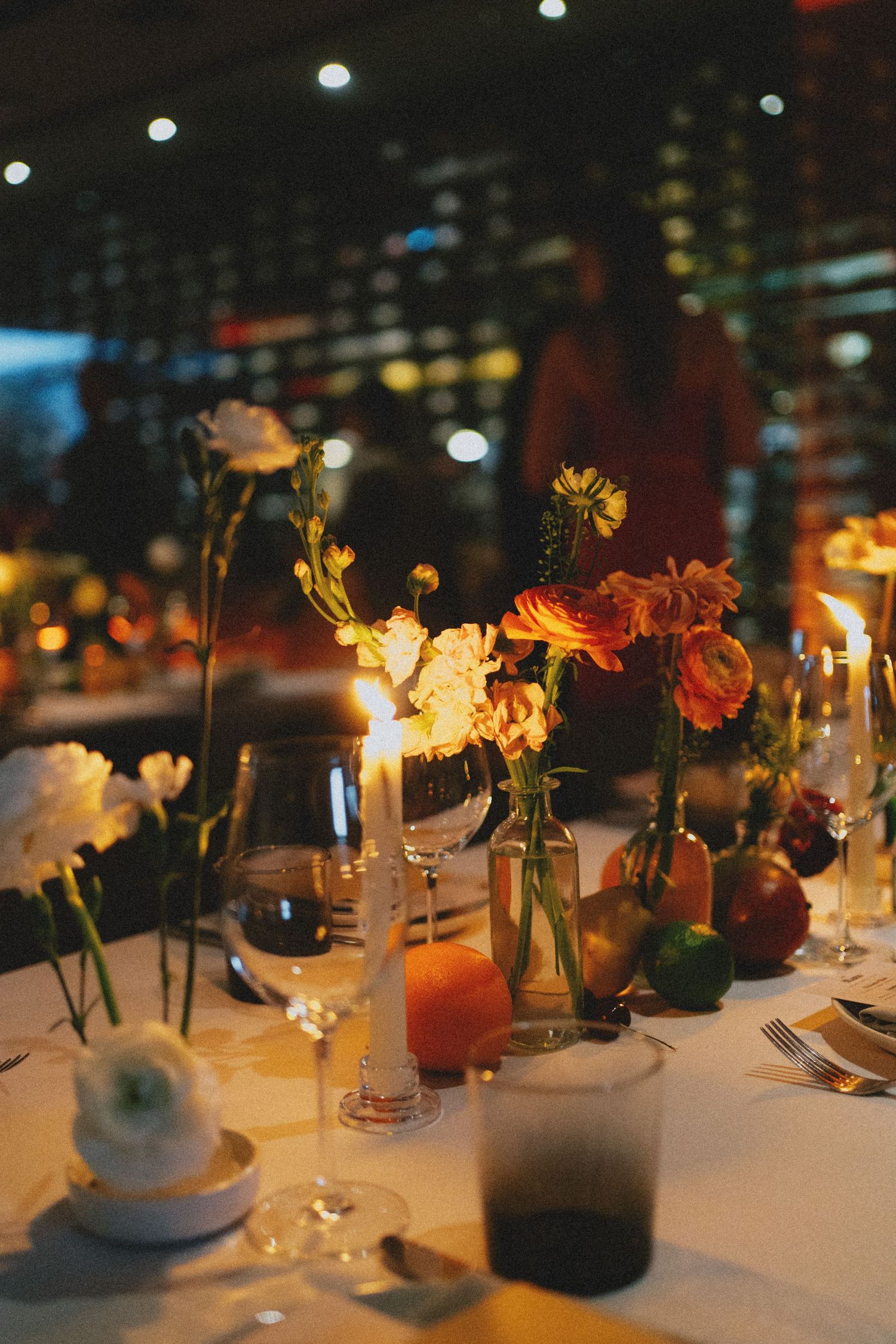 Romantic wedding reception table with candles, orange and white floral arrangements in glass vases.
