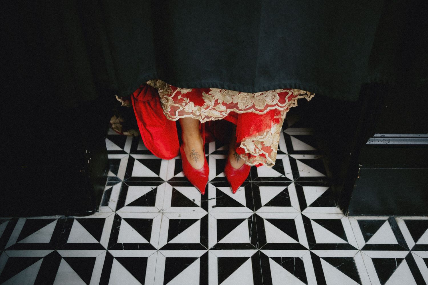 Red flamenco dress with gold trim and red shoes on black and white geometric tile floor.