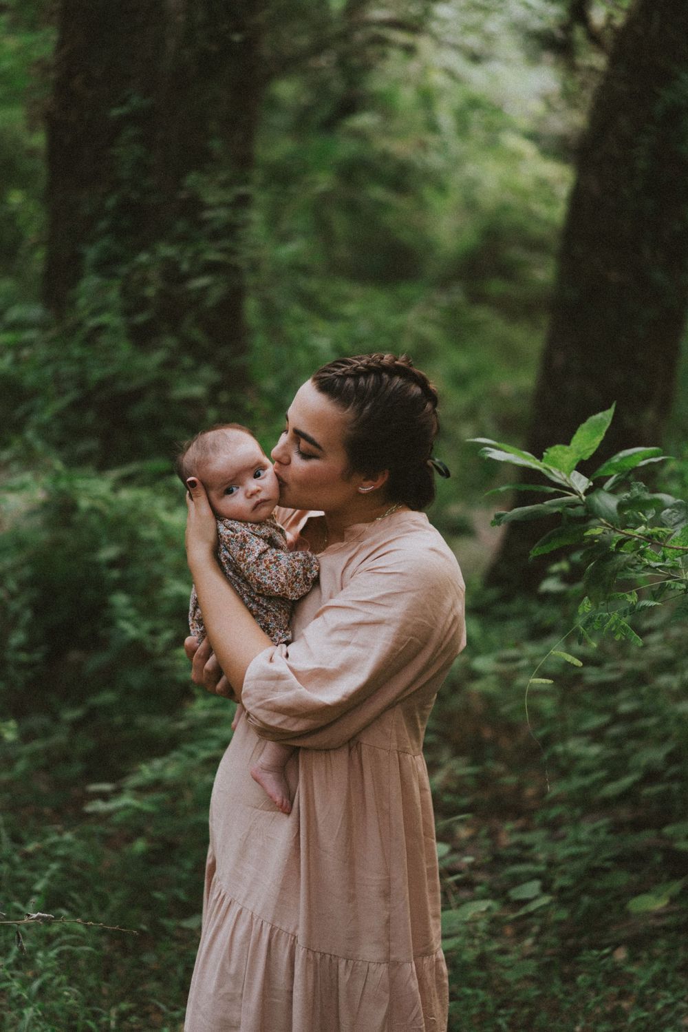A tender moment captured in a lush forest setting with soft pink tones and natural greenery.