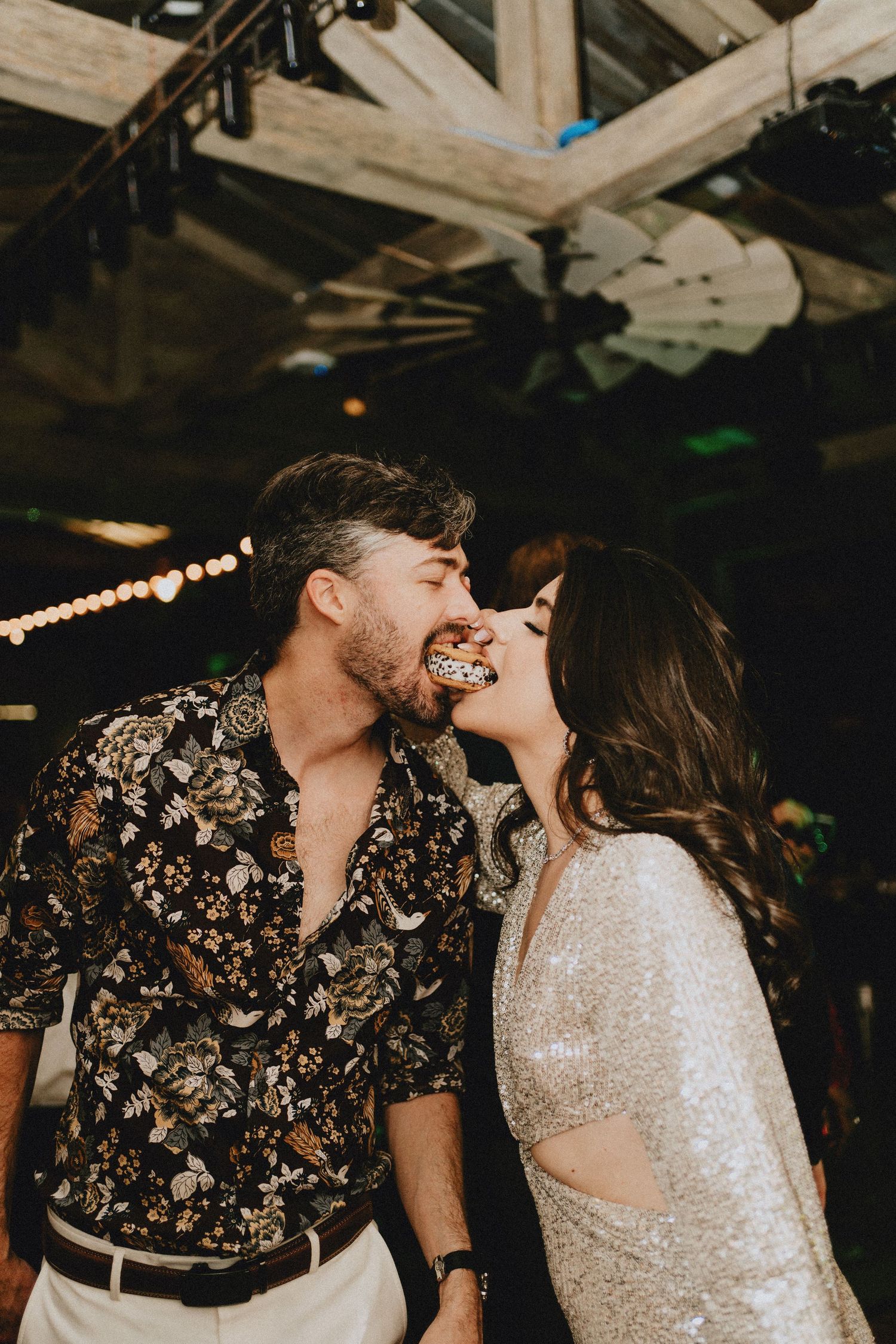 Bride and groom sharing a playful cake bite kiss on the dance floor at their wedding reception.