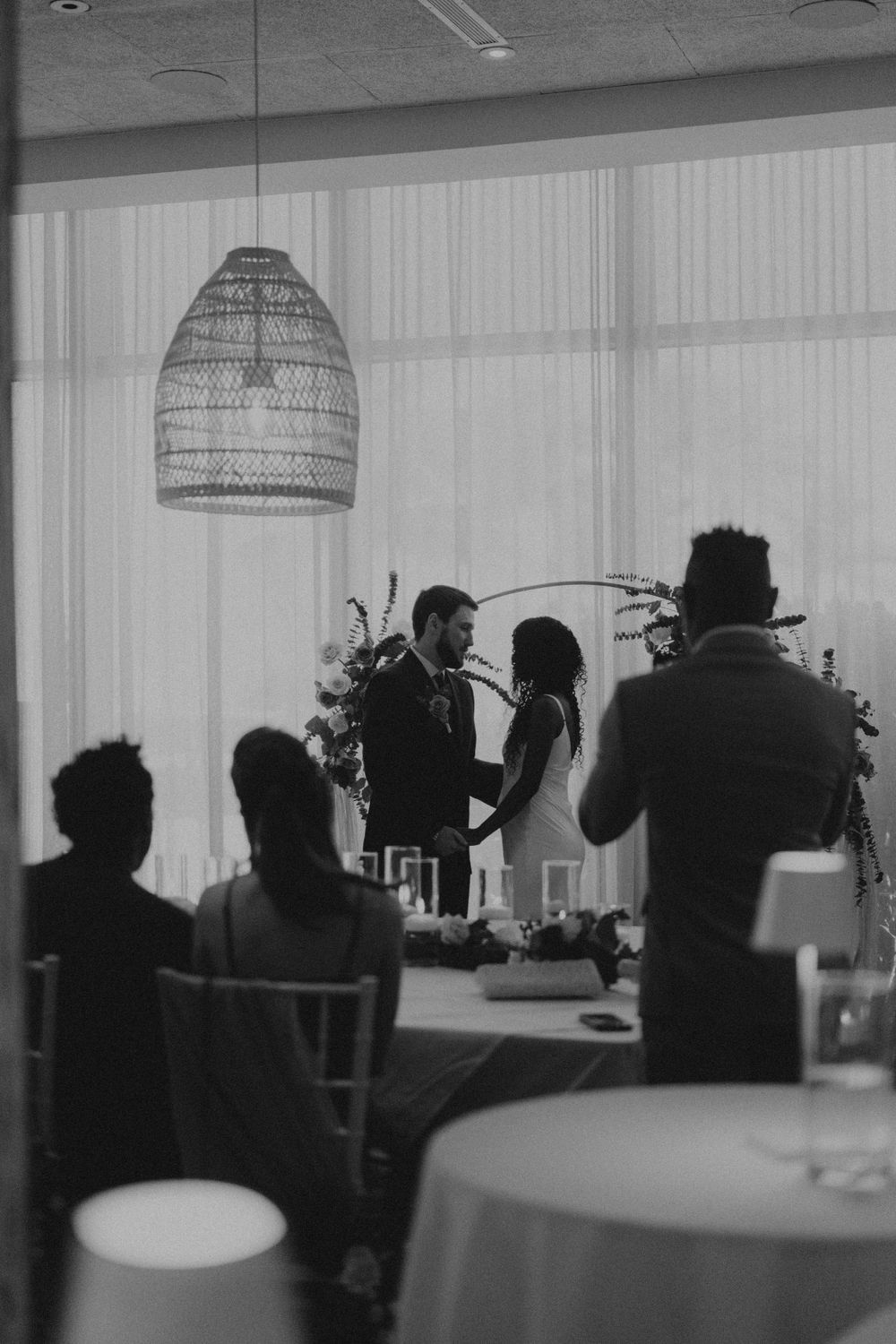 Silhouetted figures in an indoor venue with hanging pendant lights and white curtains.