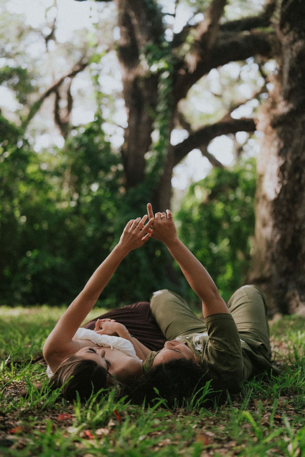 Person lying on grass reaching up towards sunlight through tree branches.