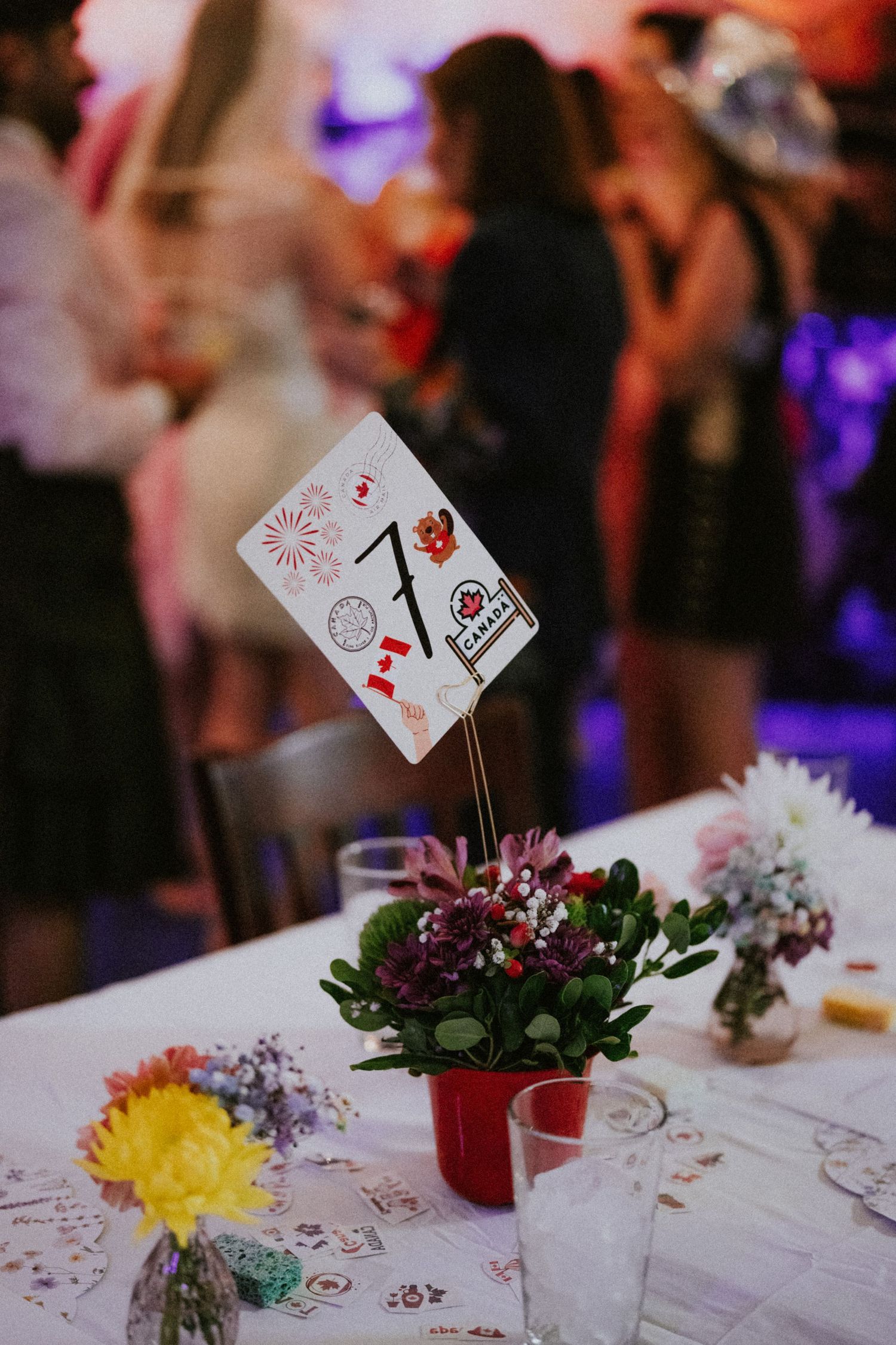 Wedding table centerpiece with table number 7, small floral arrangement, and sticker-decorated card at a reception.
