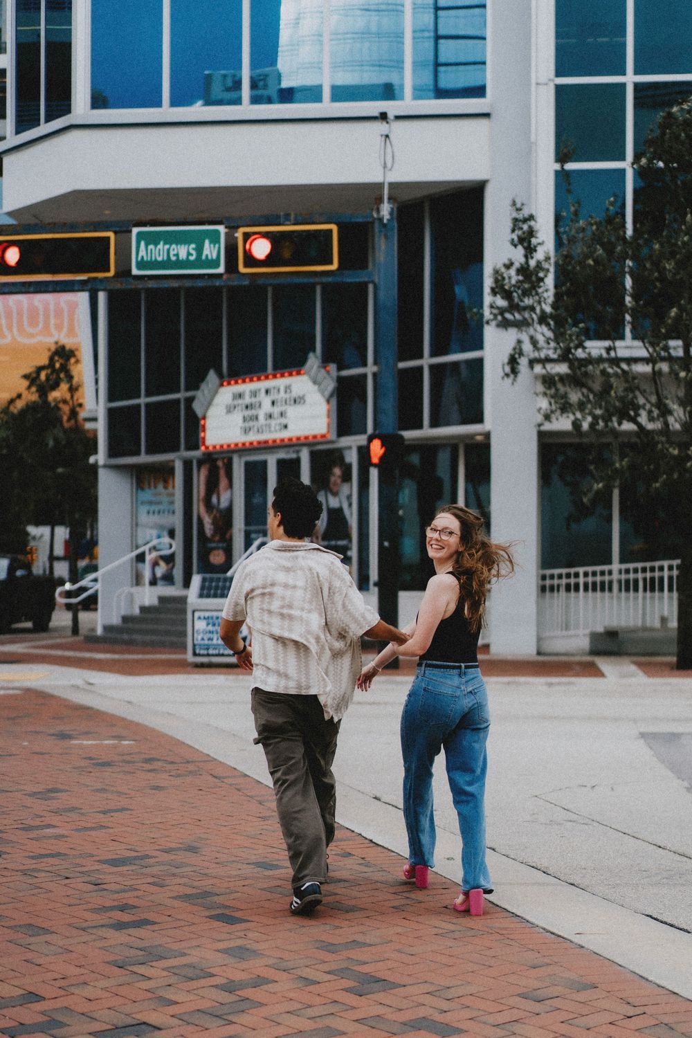 A couple walks together on a brick sidewalk in front of a city building.