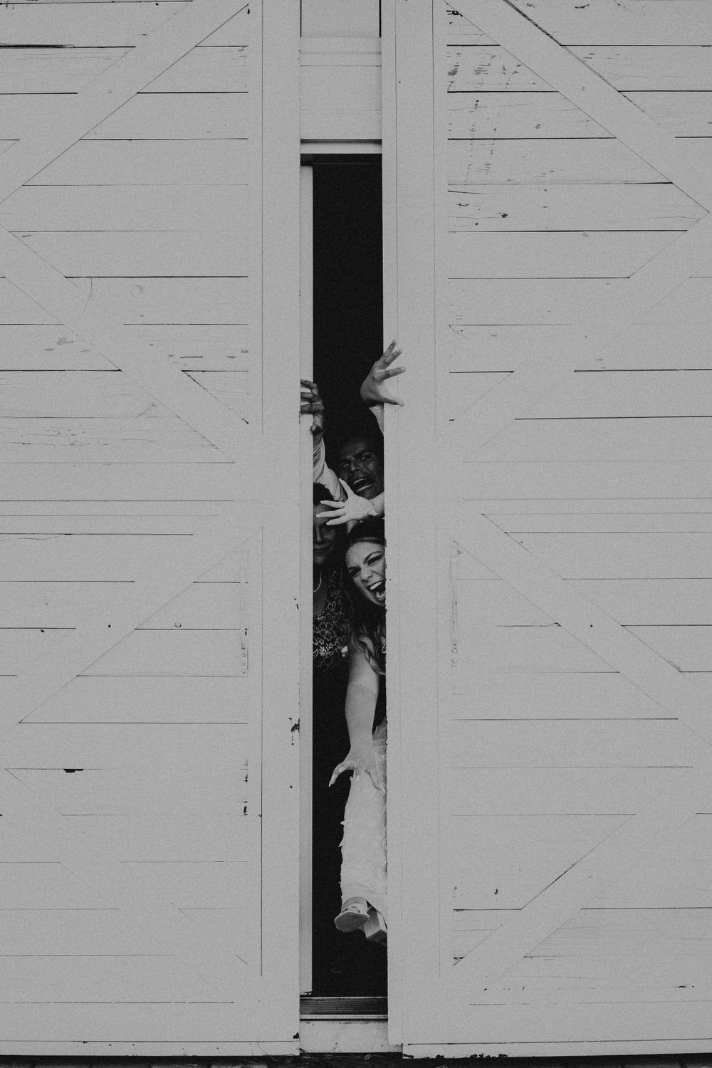 People playfully peek through gaps in white wooden barn doors.