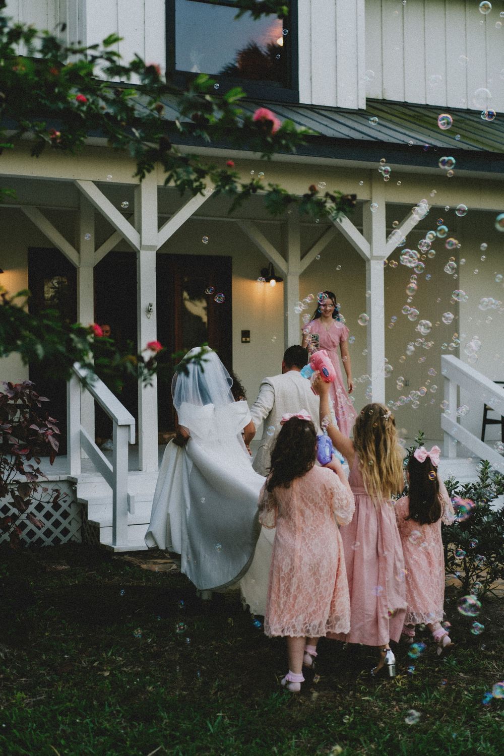 Wedding party in pink dresses playing with bubbles outside white porch.