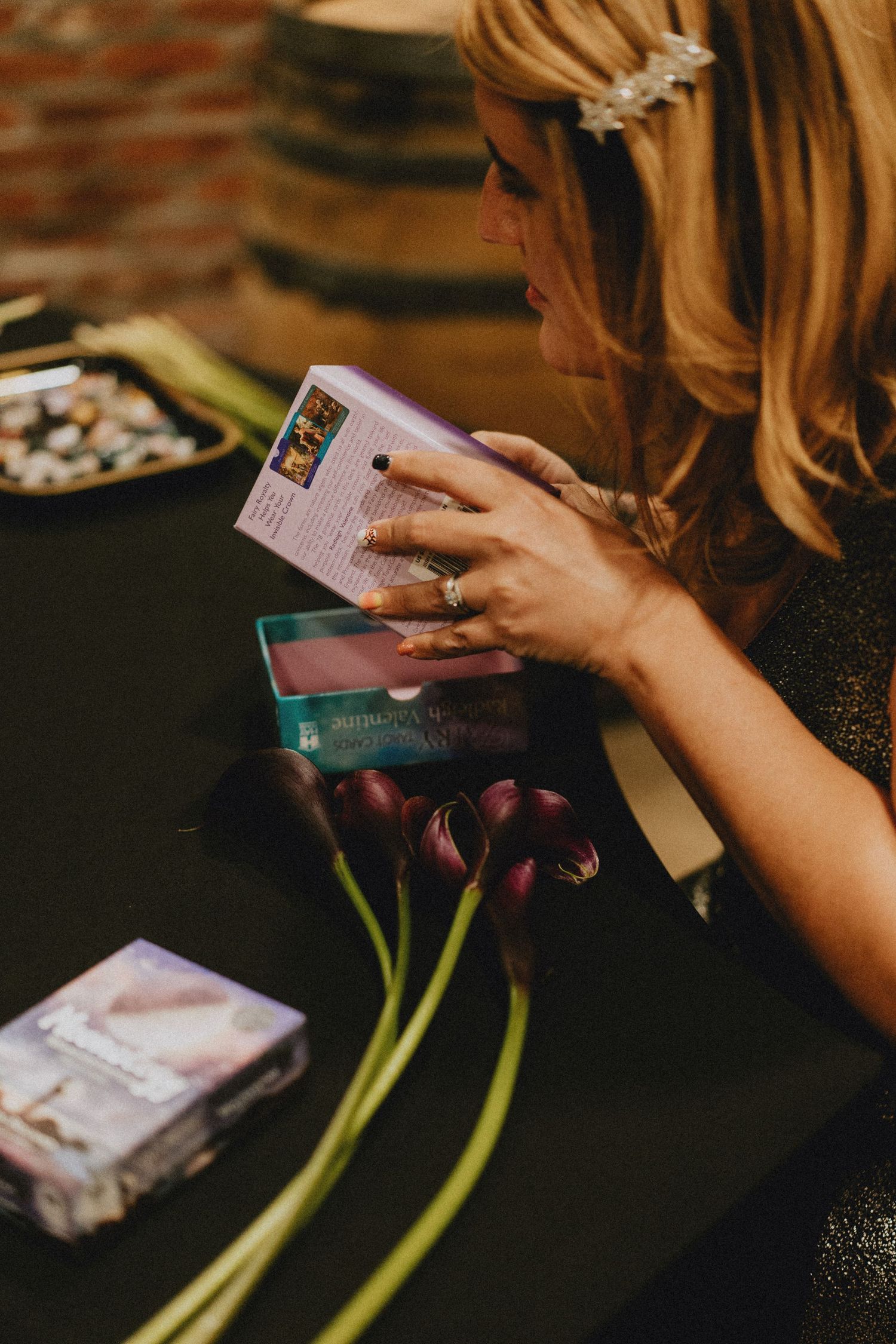 Wedding guest examines purple favor boxes beside dark calla lilies on a black tablecloth.