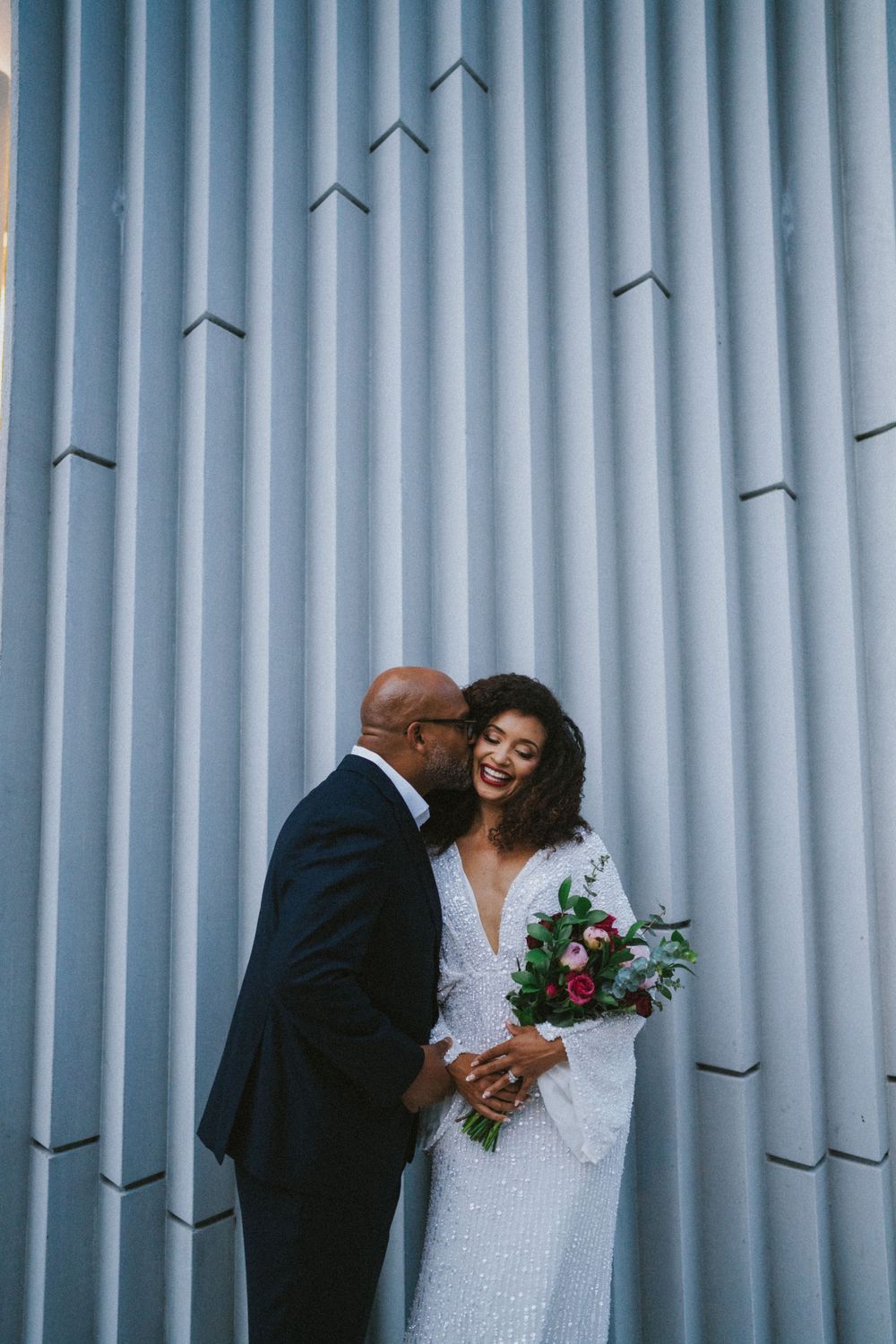 A couple sharing an intimate moment against a backdrop of geometric silver columns.