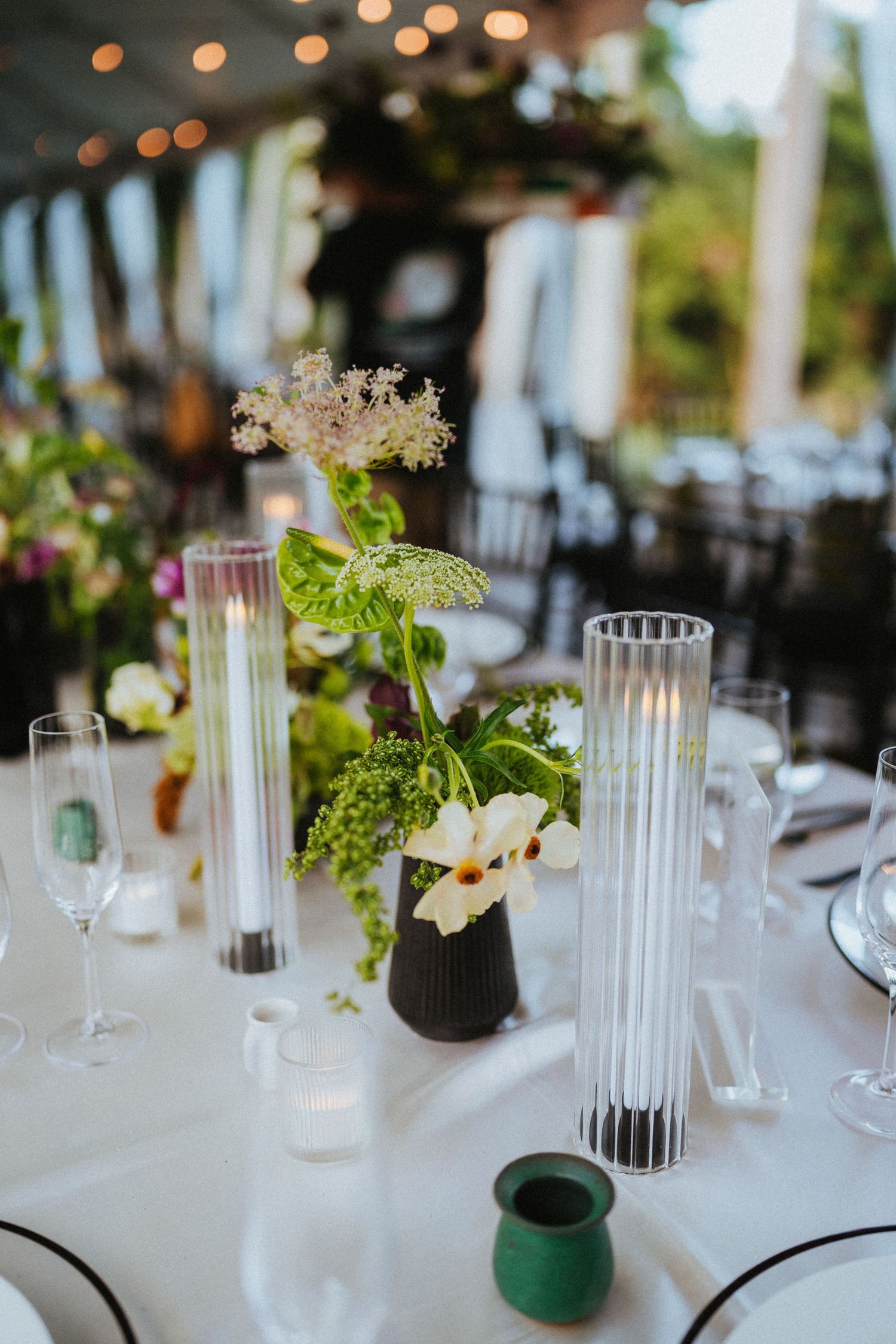 Elegant wedding reception table with white florals, green botanicals, and ribbed glass candle holders.