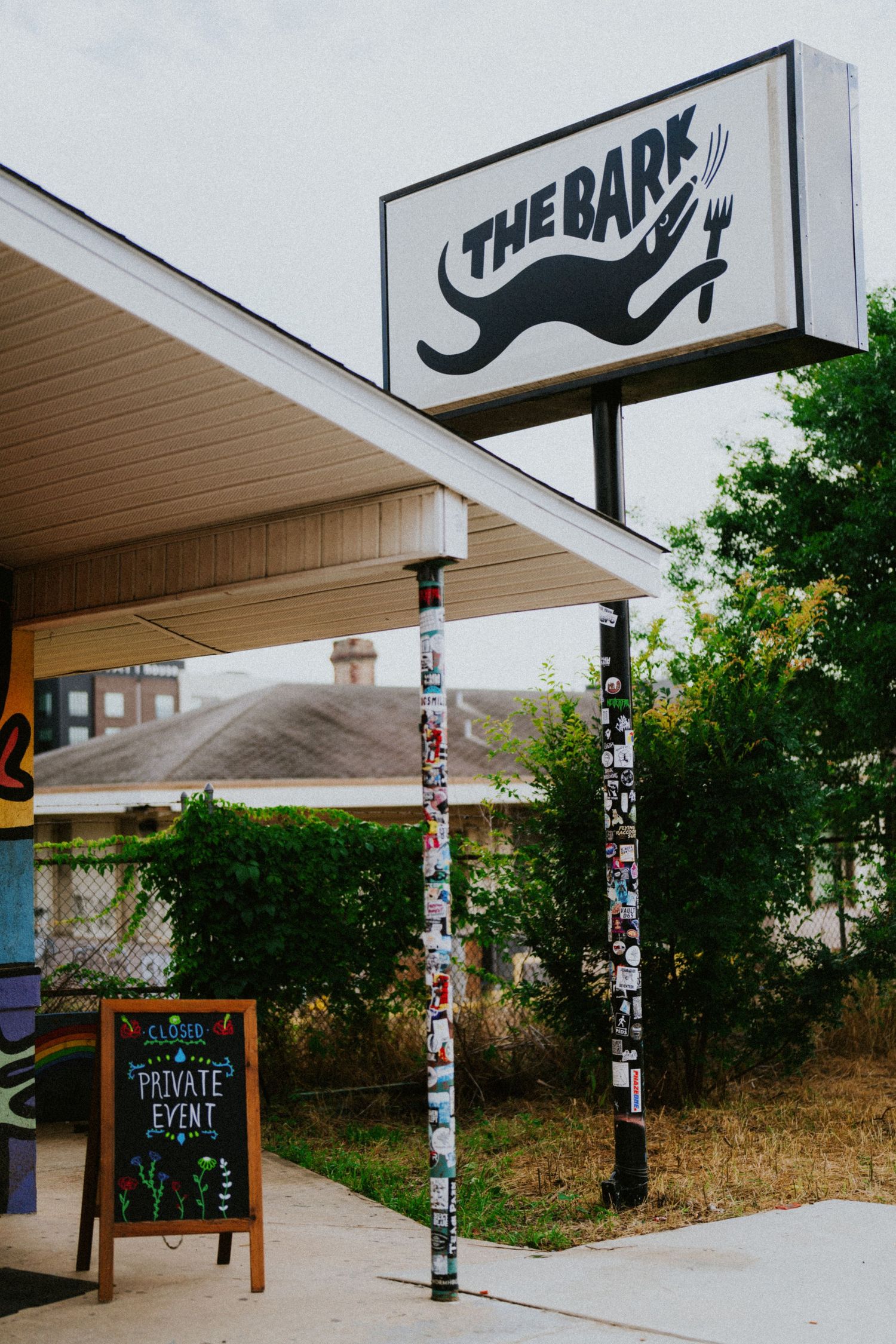 The Bark restaurant exterior sign with a private event chalkboard sign and colorful sticker-covered poles.