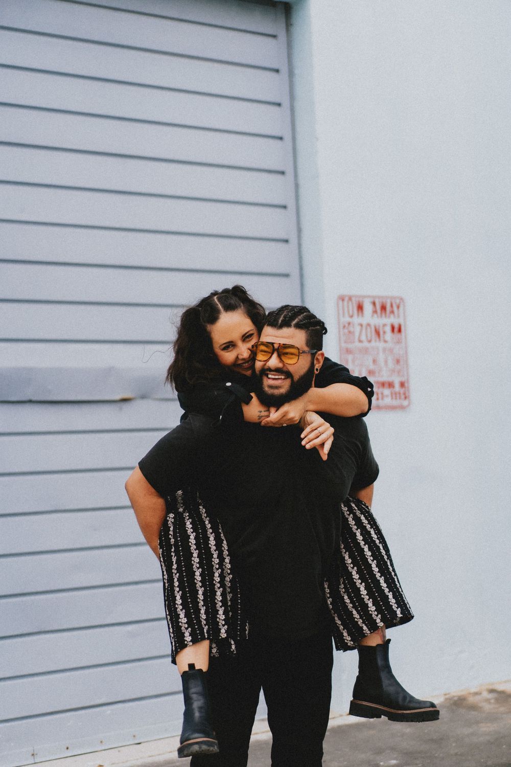 Couple embracing in front of white garage door in casual urban setting.