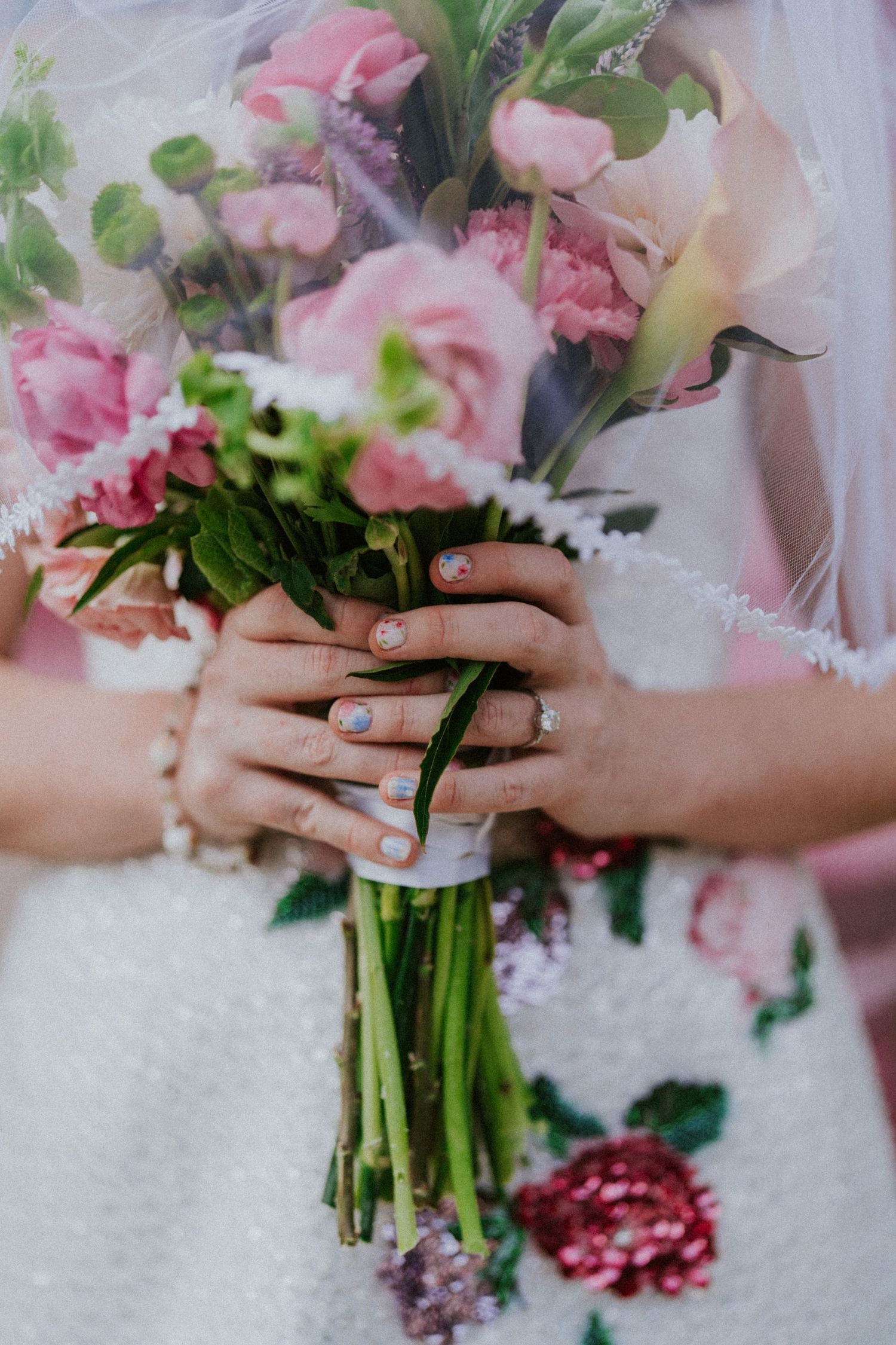 Close-up of hands holding a delicate pink and white wedding bouquet with painted nails.