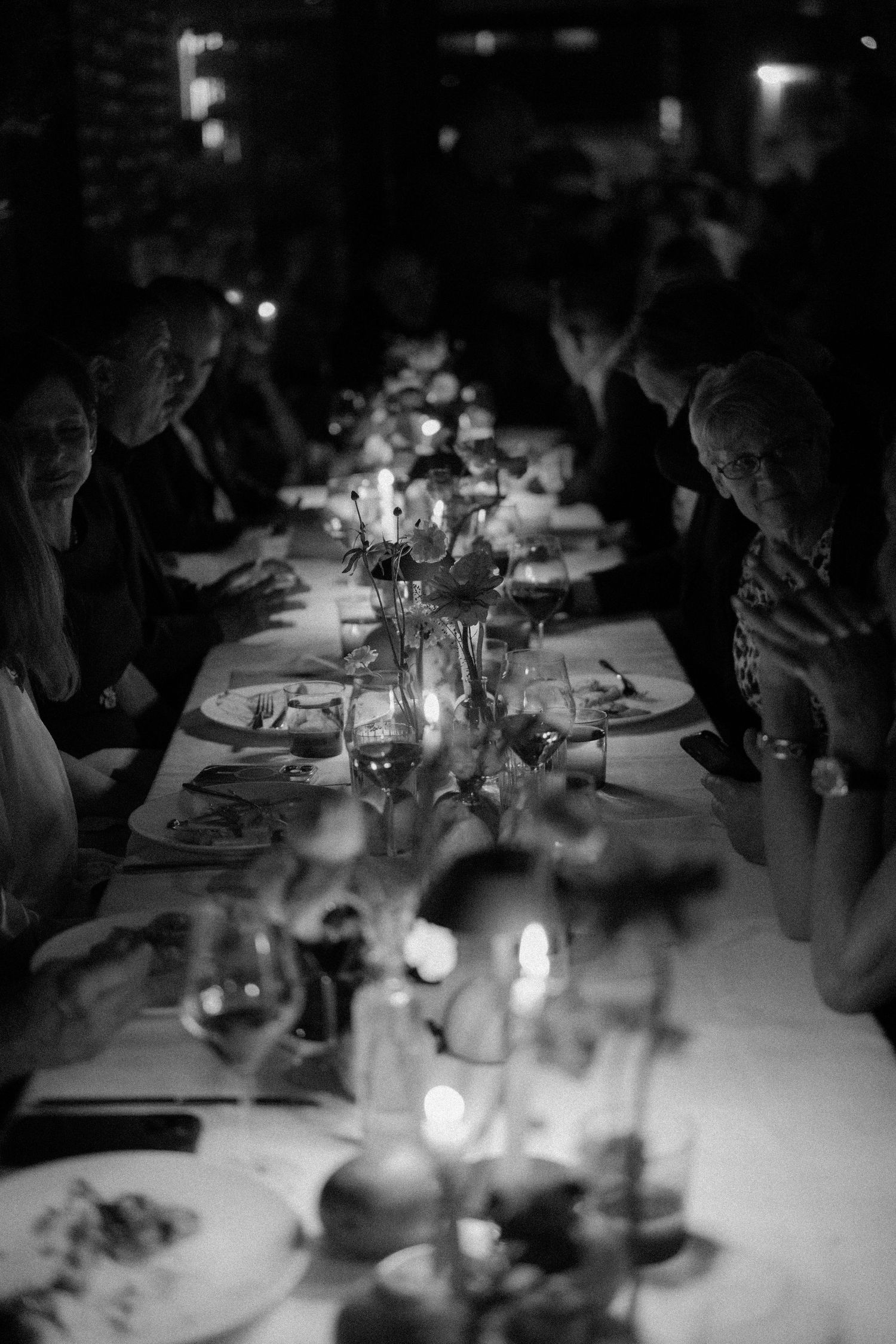 Elegant candlelit wedding reception dinner table with guests seated in black and white photo.