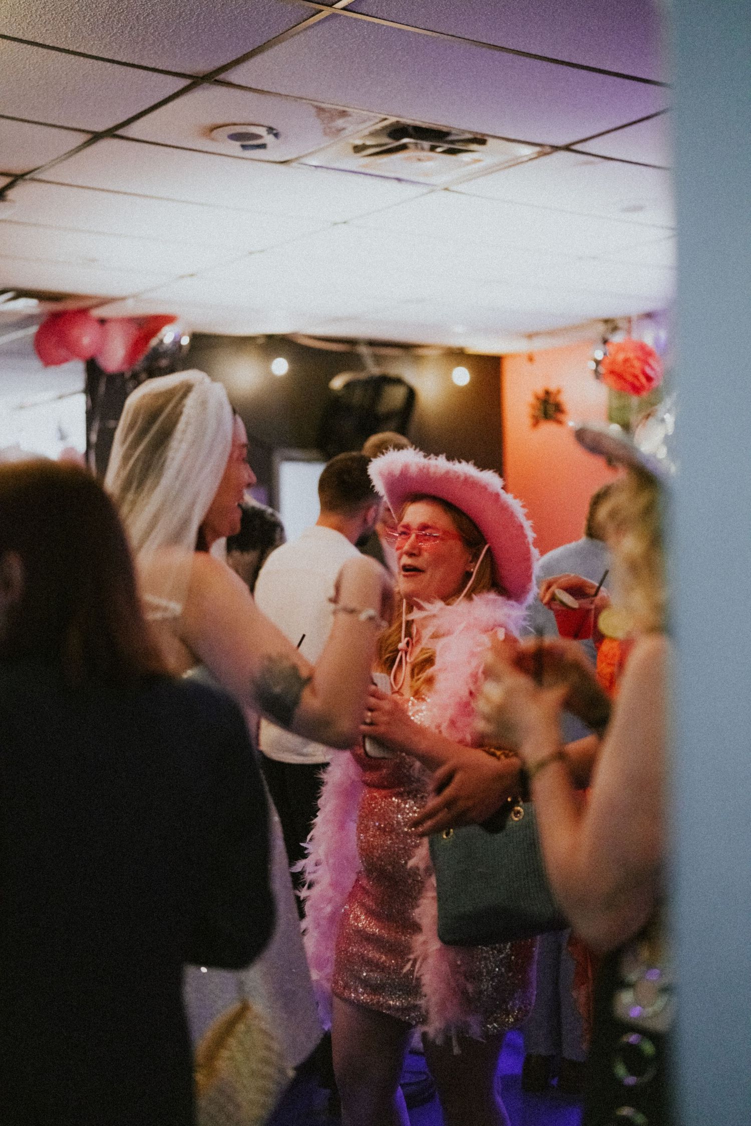 Woman in pink feather boa and cowboy hat laughing at a lively indoor party with festive decorations.