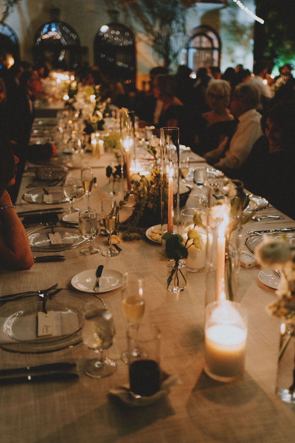 Elegant wedding reception table set with glowing candles, fine china, and glassware in a romantic evening setting.