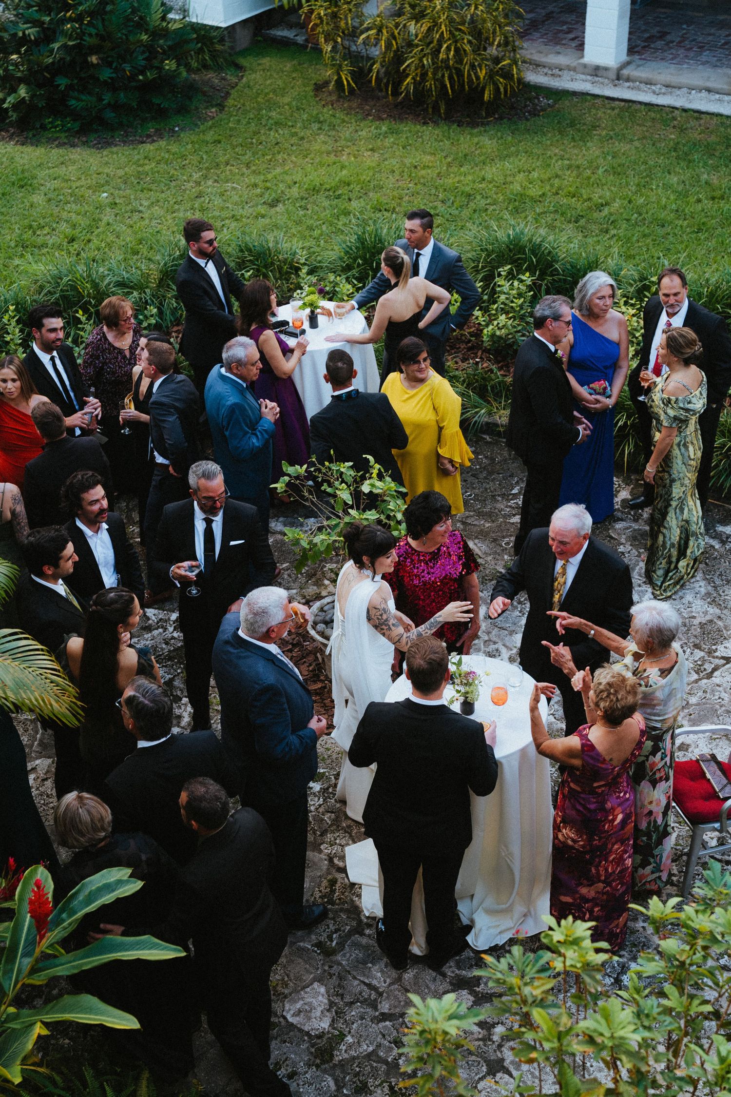 Aerial view of elegantly dressed wedding guests mingling outdoors in a lush garden reception venue.