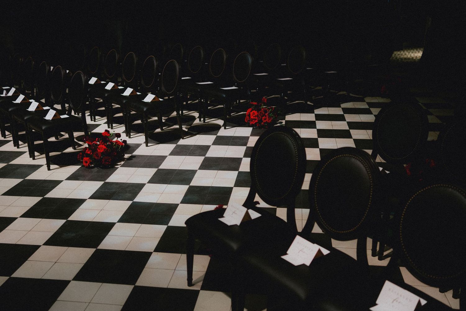 Elegant black chairs on a checkered floor with red floral accents in a dimly lit theater setting.